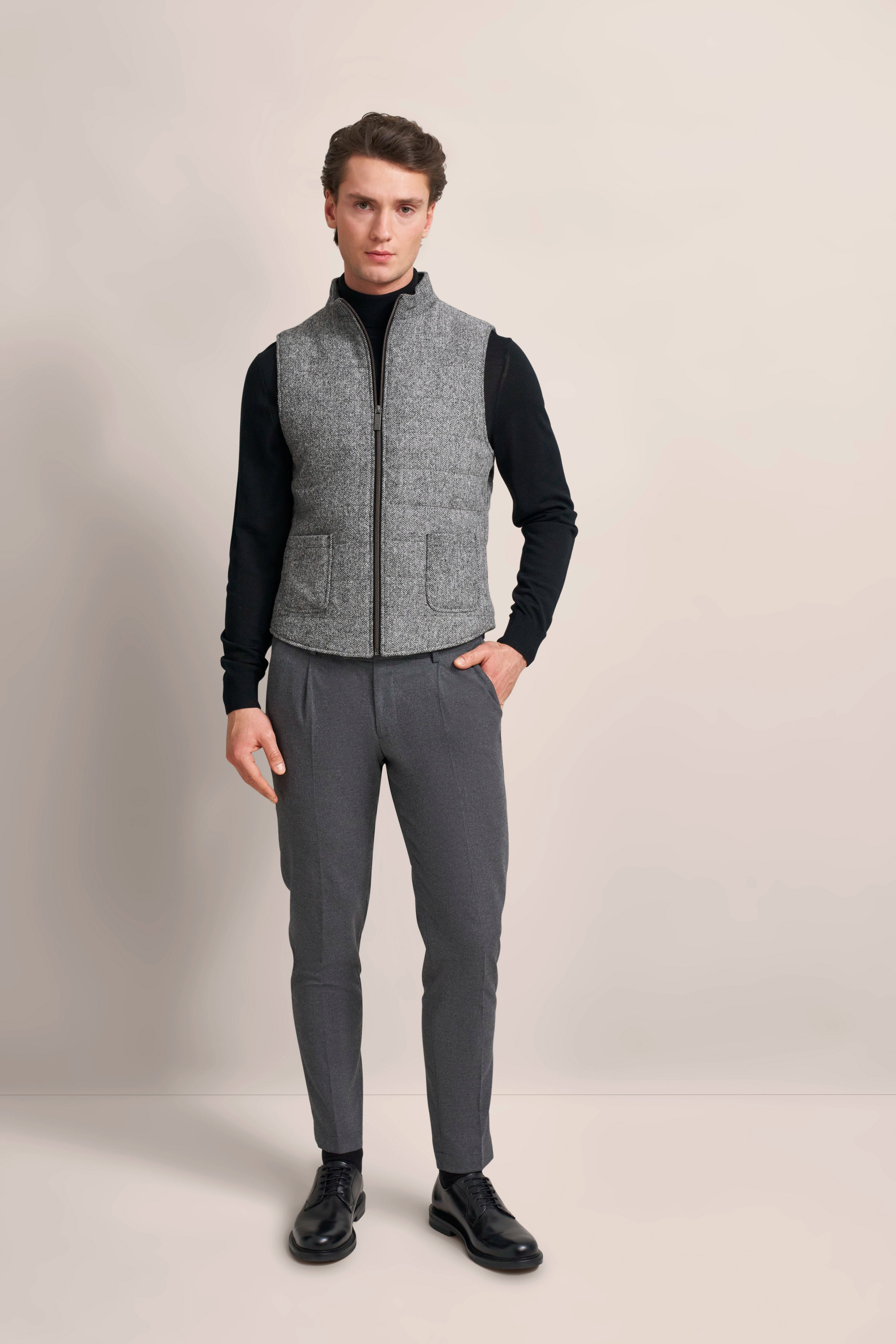Graue Tweed-Weste über schwarzem Pullover, graue Hose, Rückansicht, Modelbild stehend.