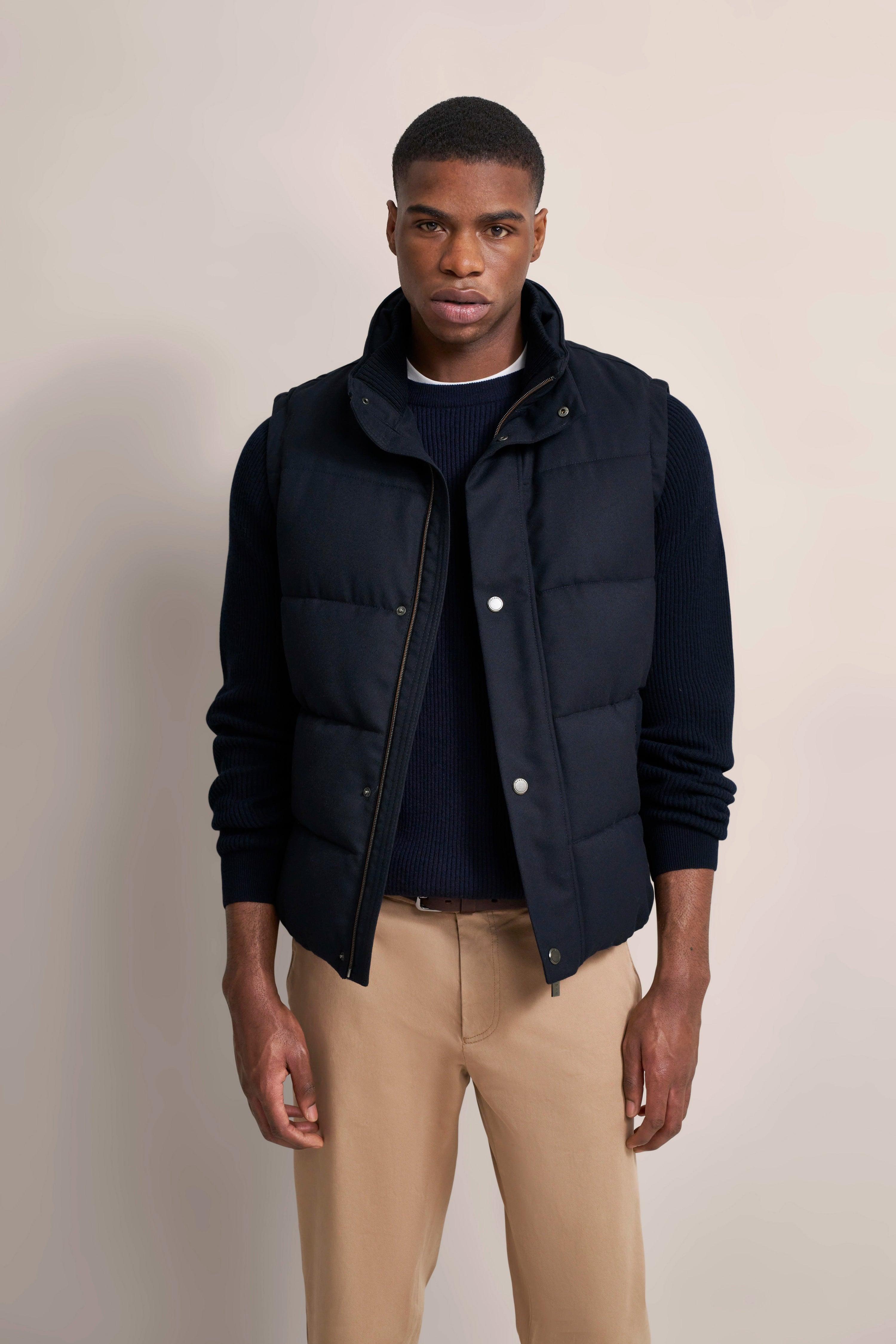 Model in bugatti Outfit: Dunkelblaue Weste, Pullover, beige Chinos, frontale Pose, entspannter Stil.