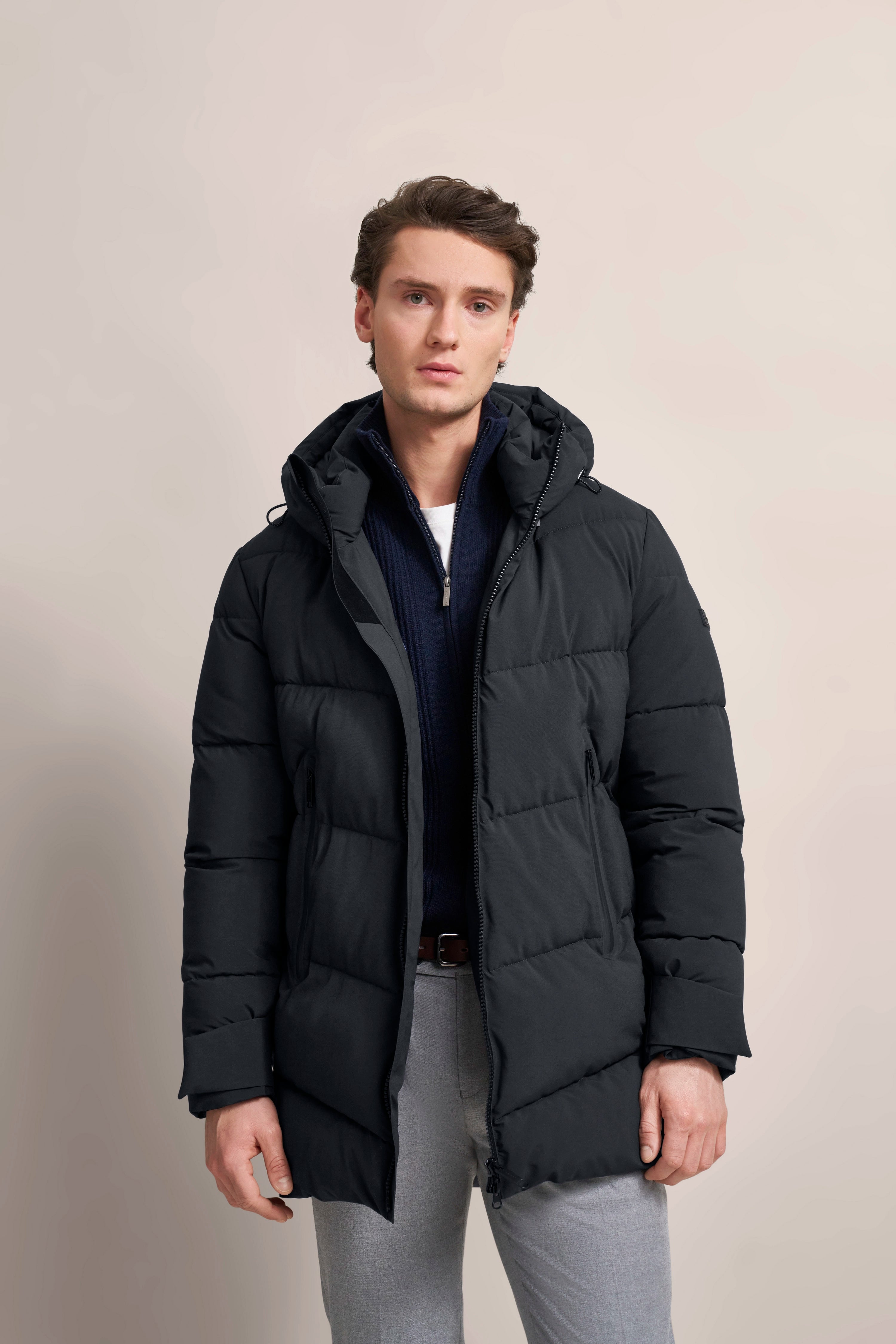Model in schwarzem bugatti Parka, dunkelblauer Pullover, graue Hose, entspannte Pose.