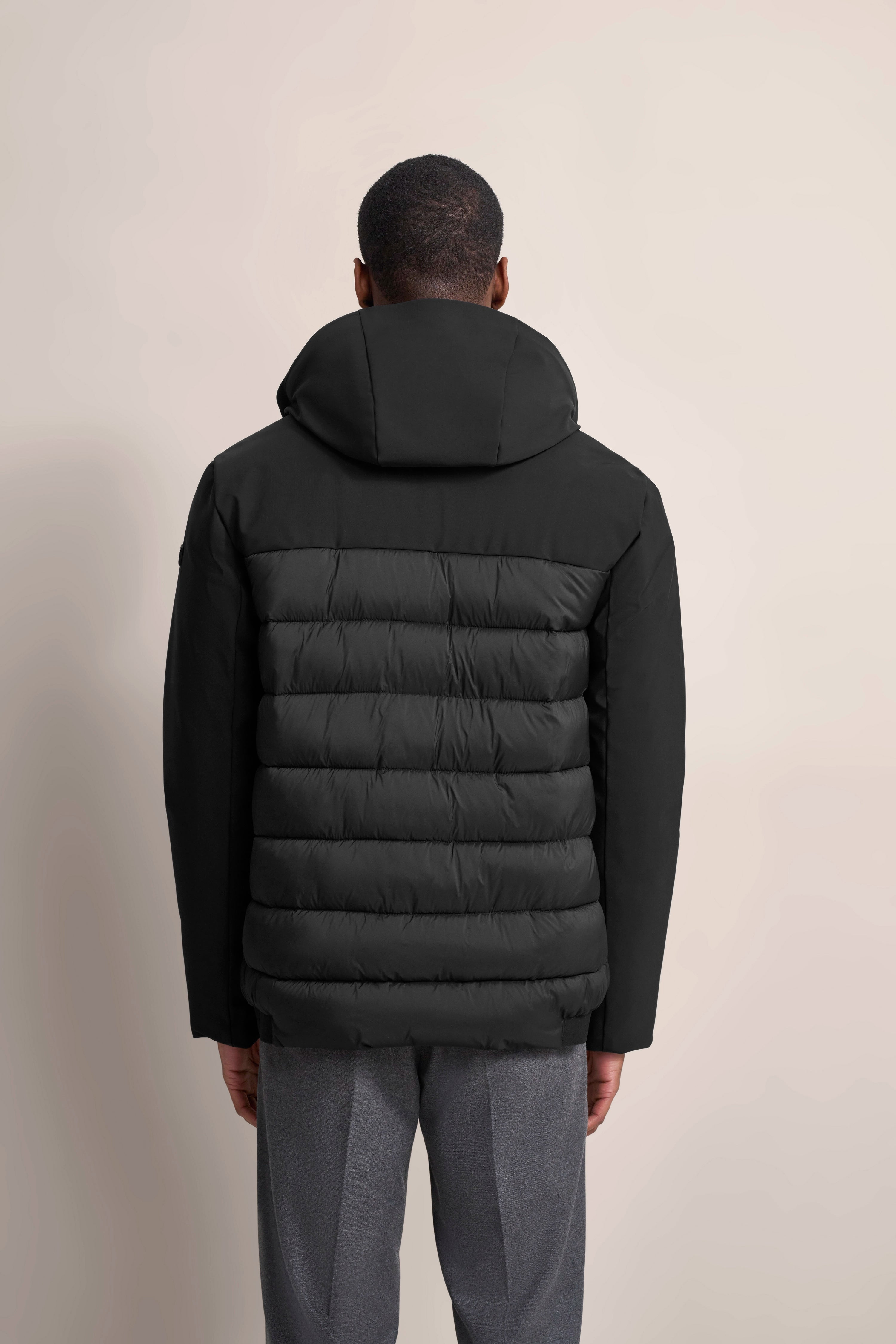 Rückansicht eines schwarzen bugatti Steppjacke auf Model, graue Hose, entspanntes Posing.