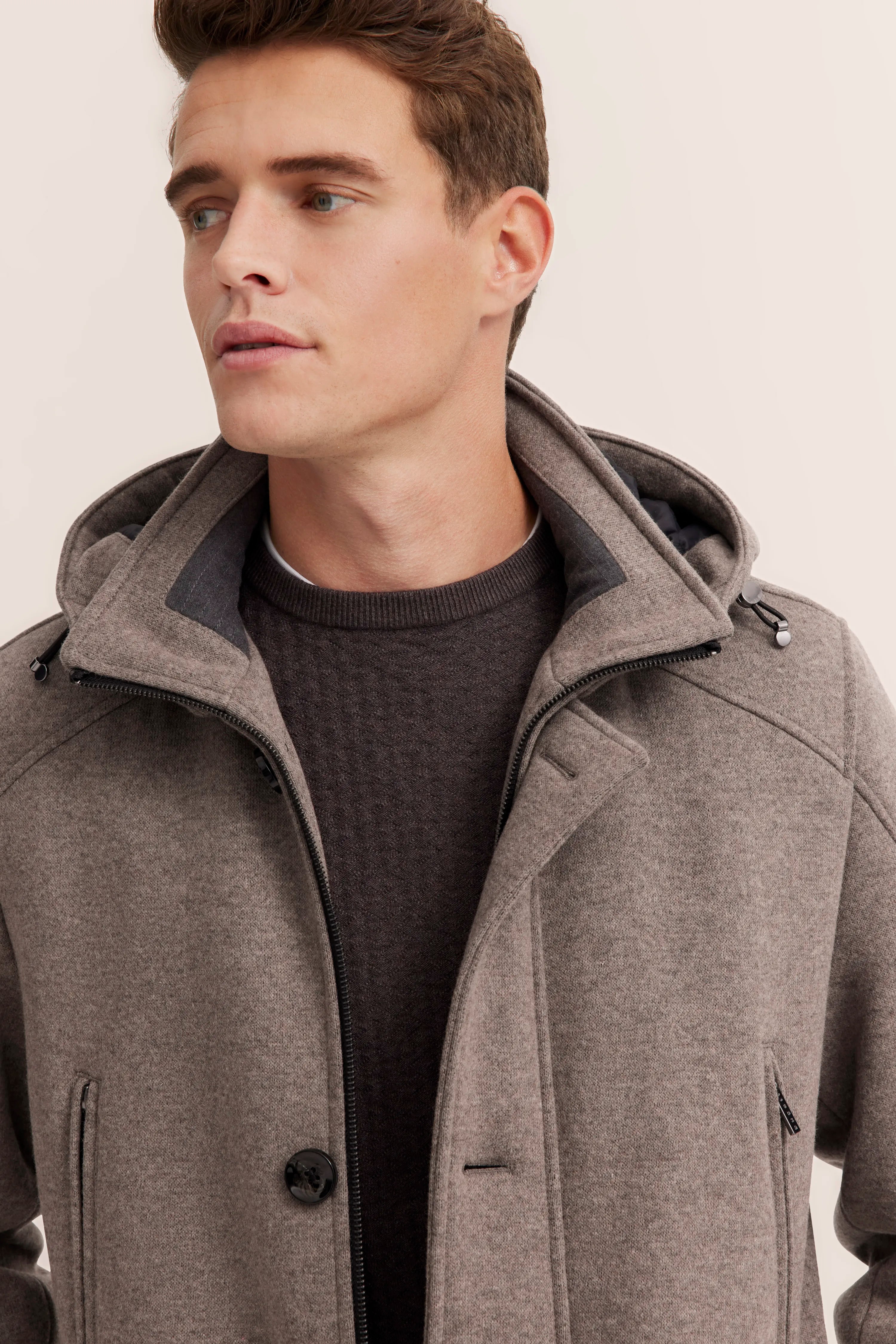 Model in grauem bugatti Mantel mit Kapuze, darunter ein brauner Pullover. Legeres Posing.