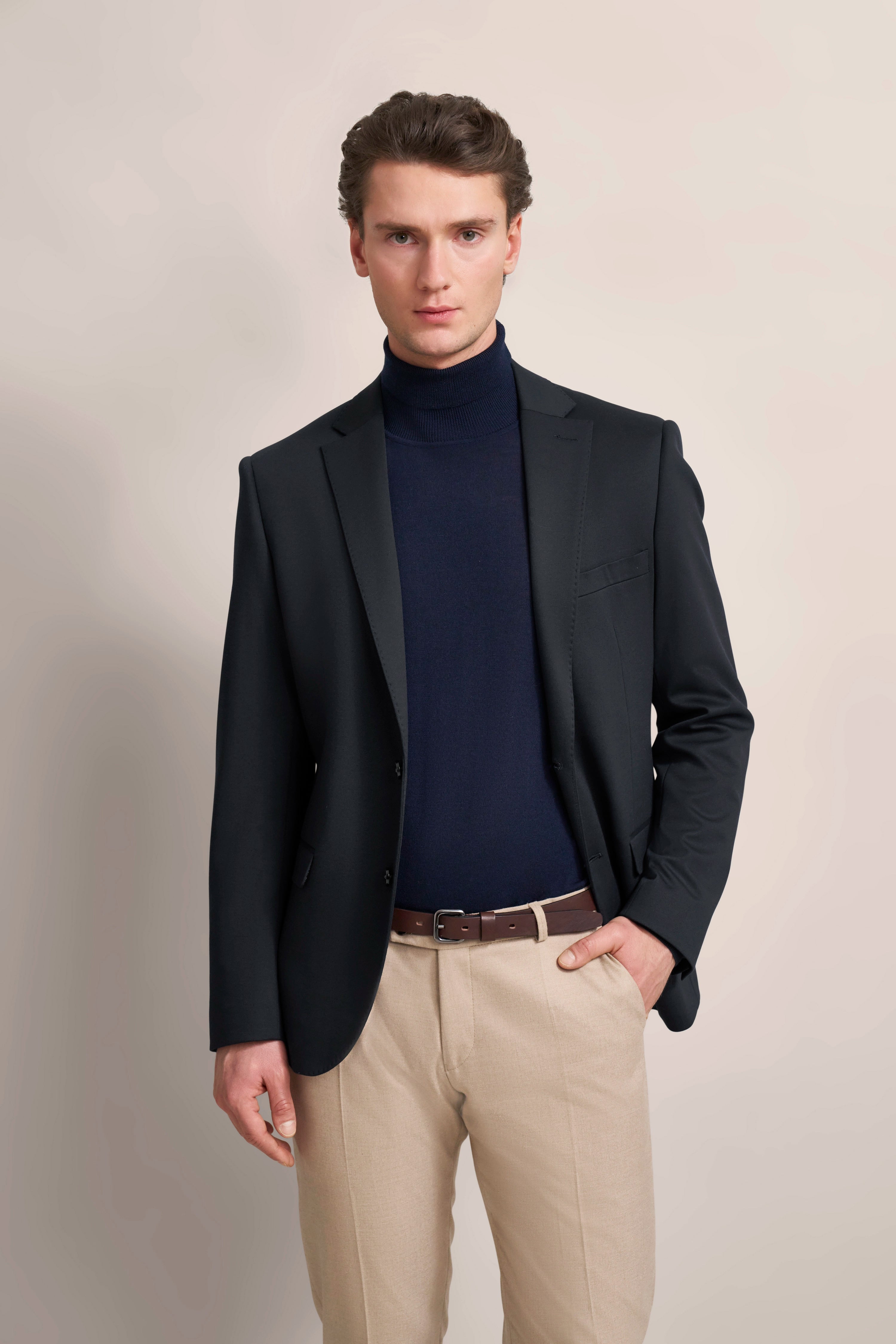 Model in bugatti outfit: black blazer, dark blue turtleneck, beige trousers