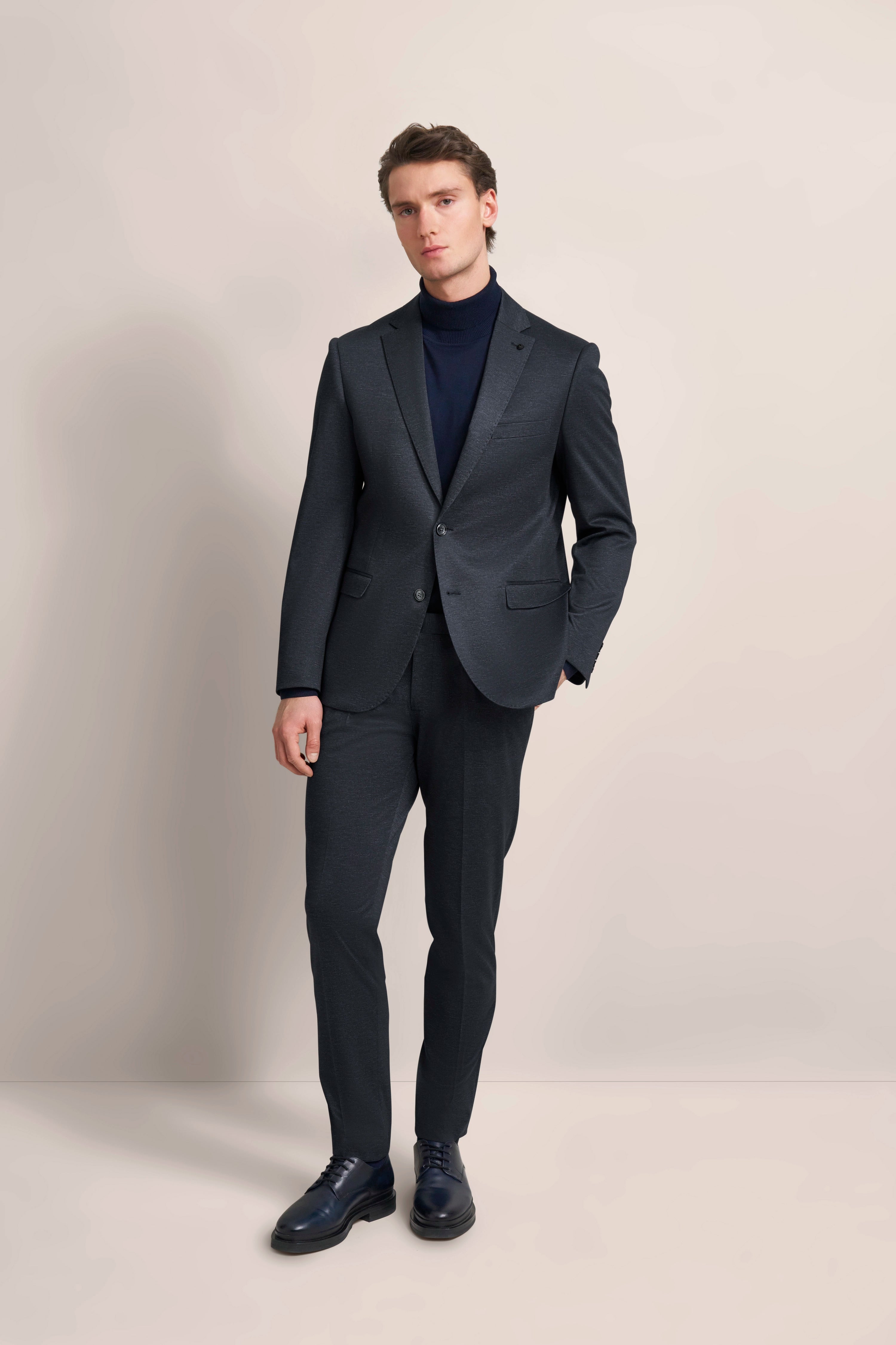Dark suit with blue turtleneck, elegant model, casual pose with hand in pocket.