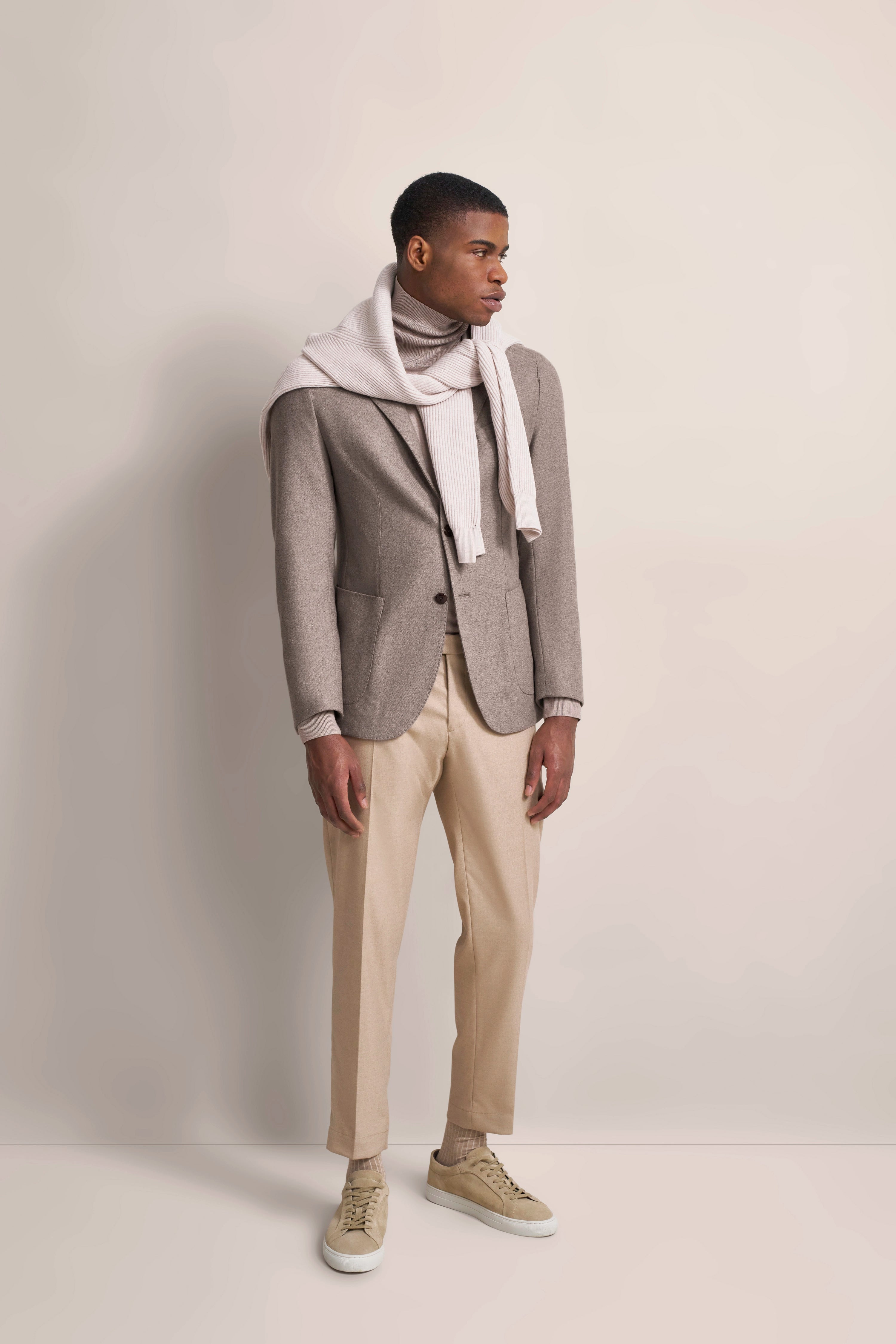 Elegant bugatti outfit: gray blazer, beige turtleneck, scarf, light pants, model in relaxed pose.