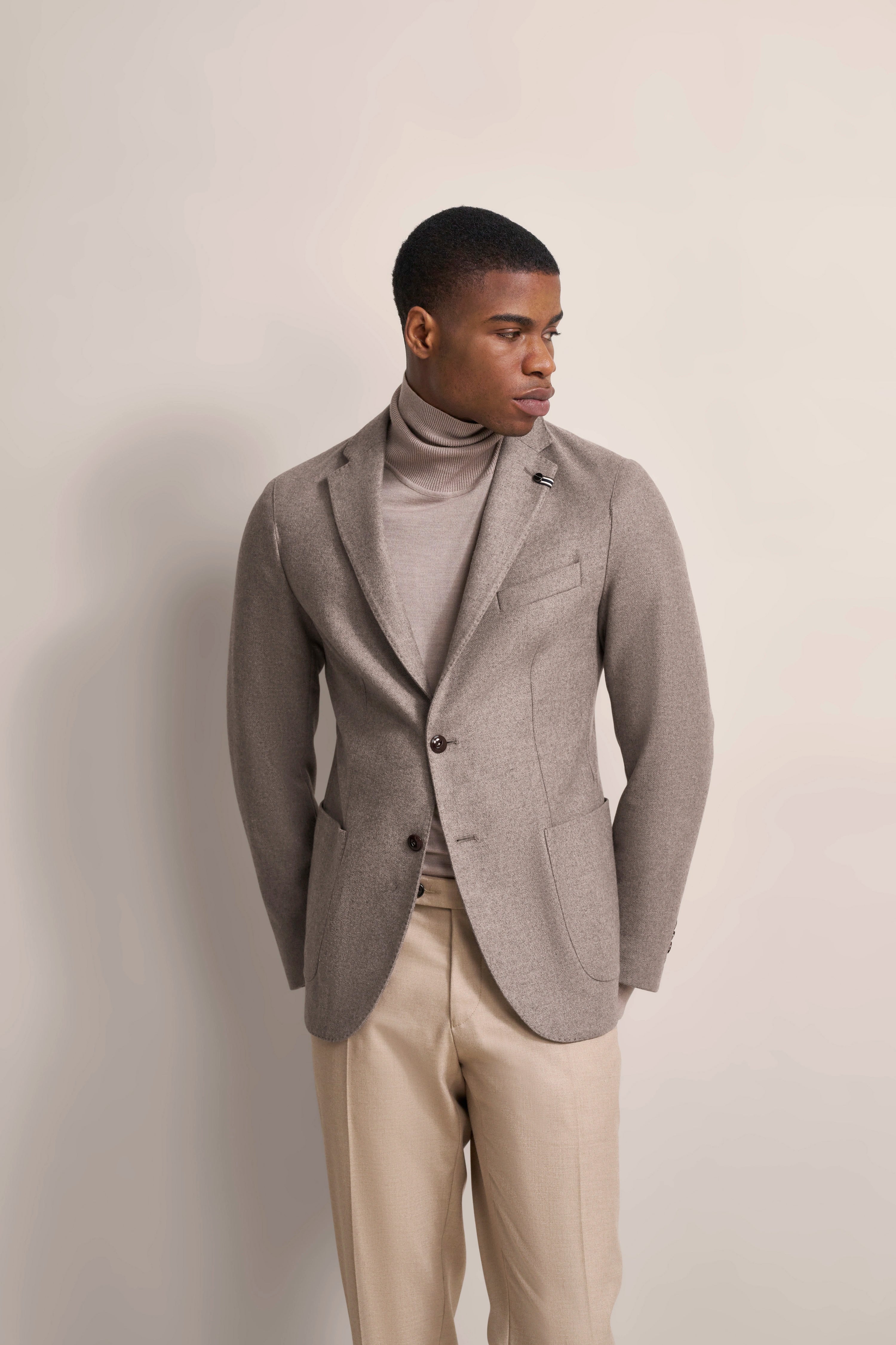 Gray bugatti suit with turtleneck, beige pants, model posing sideways.