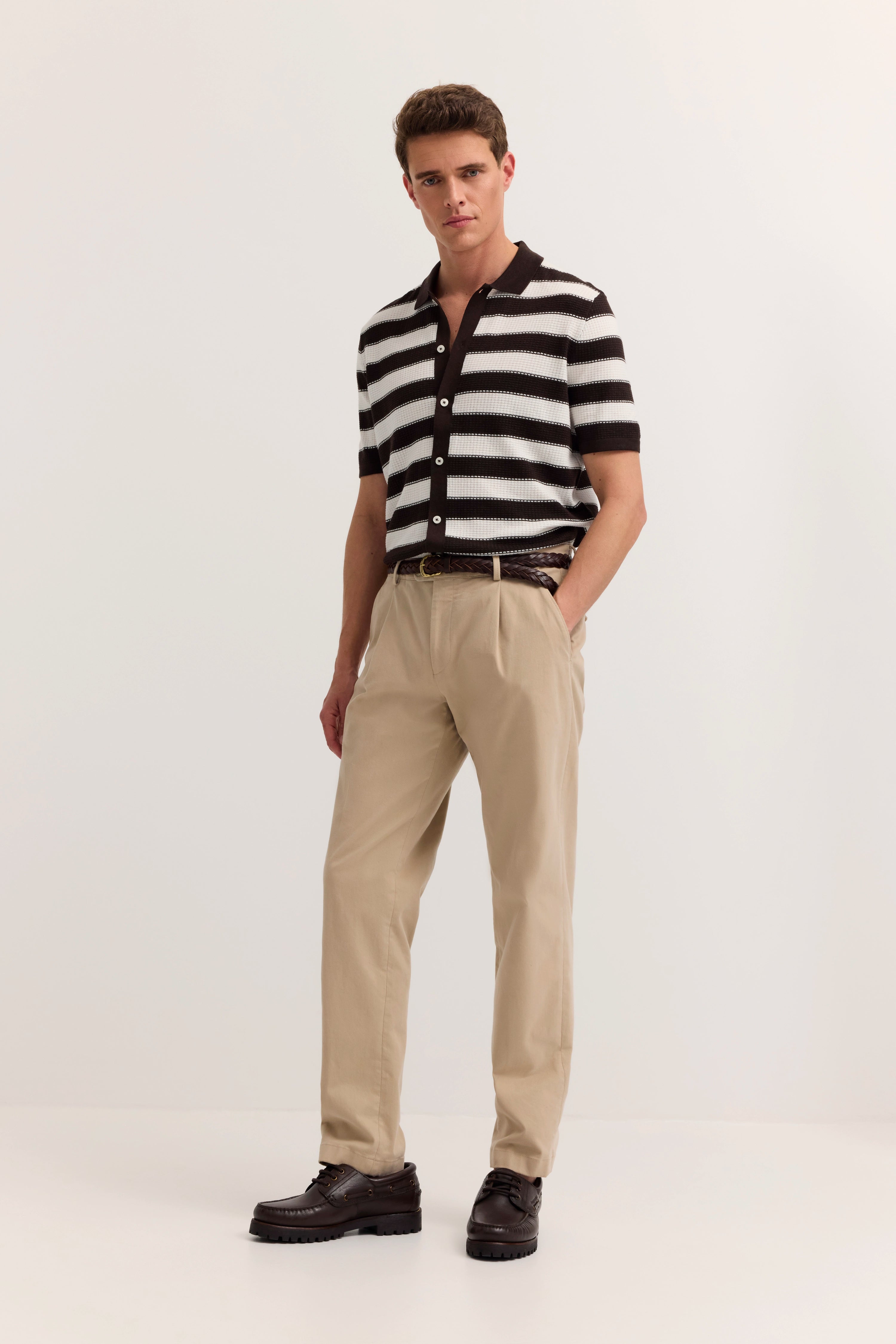 Model in gestreiftem Polohemd und beigen Chinos von bugatti, lässiger Stand.