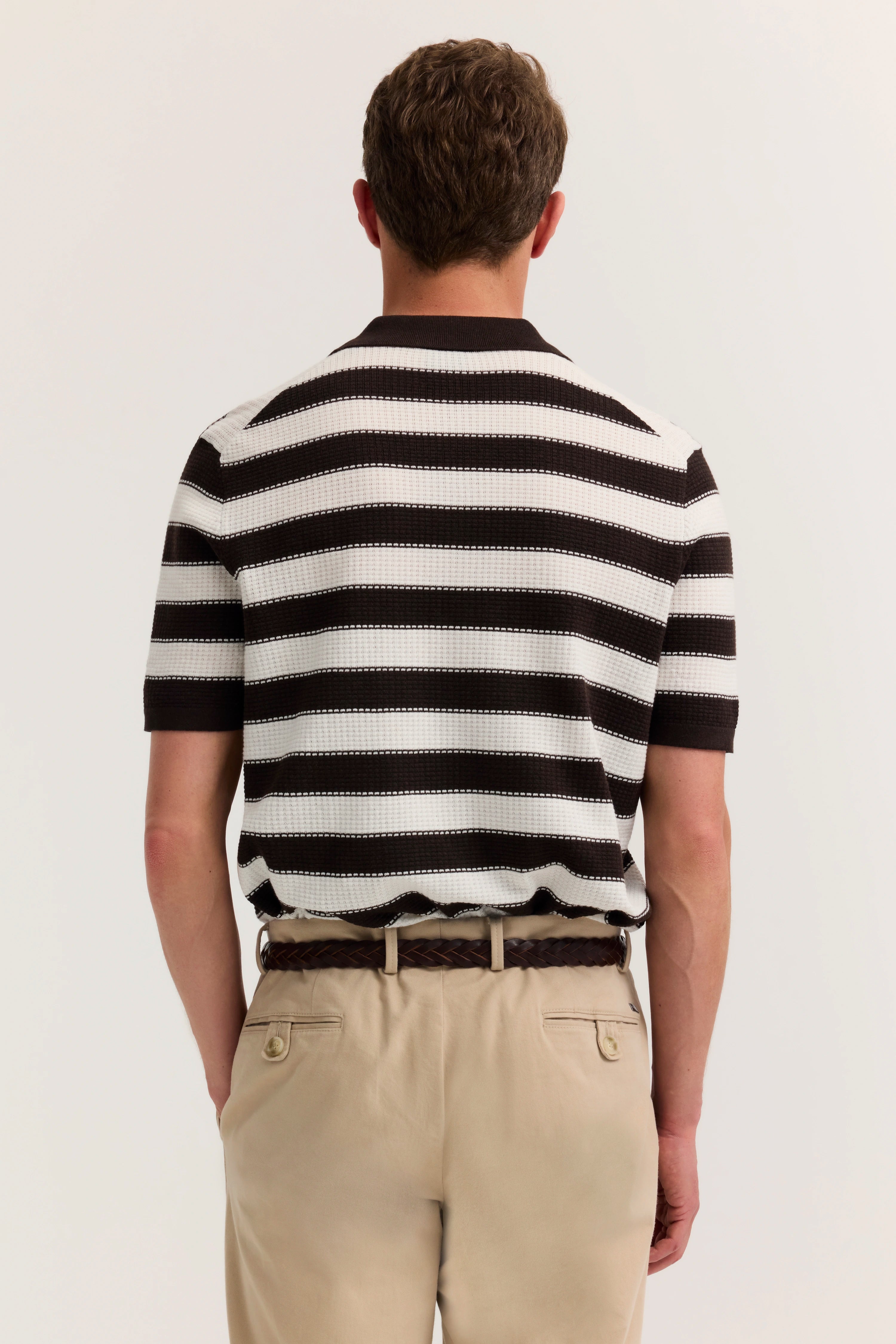 Rückansicht Model, gestreiftes Polo in Schwarz-Weiß, beige Hose, entspannte Pose.