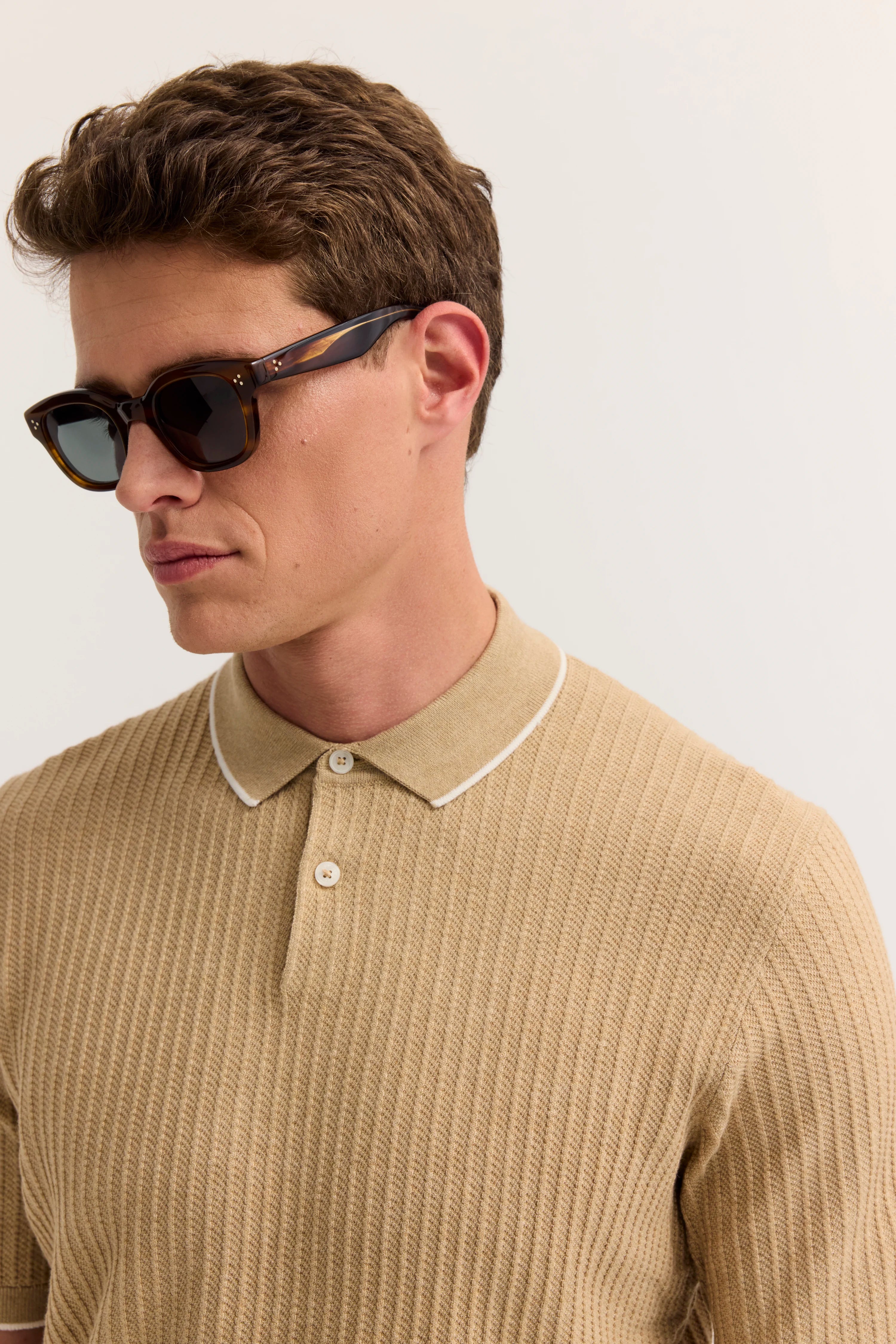Beiges Polohemd mit Strukturmuster, Model trägt Sonnenbrille, Halbprofilansicht.