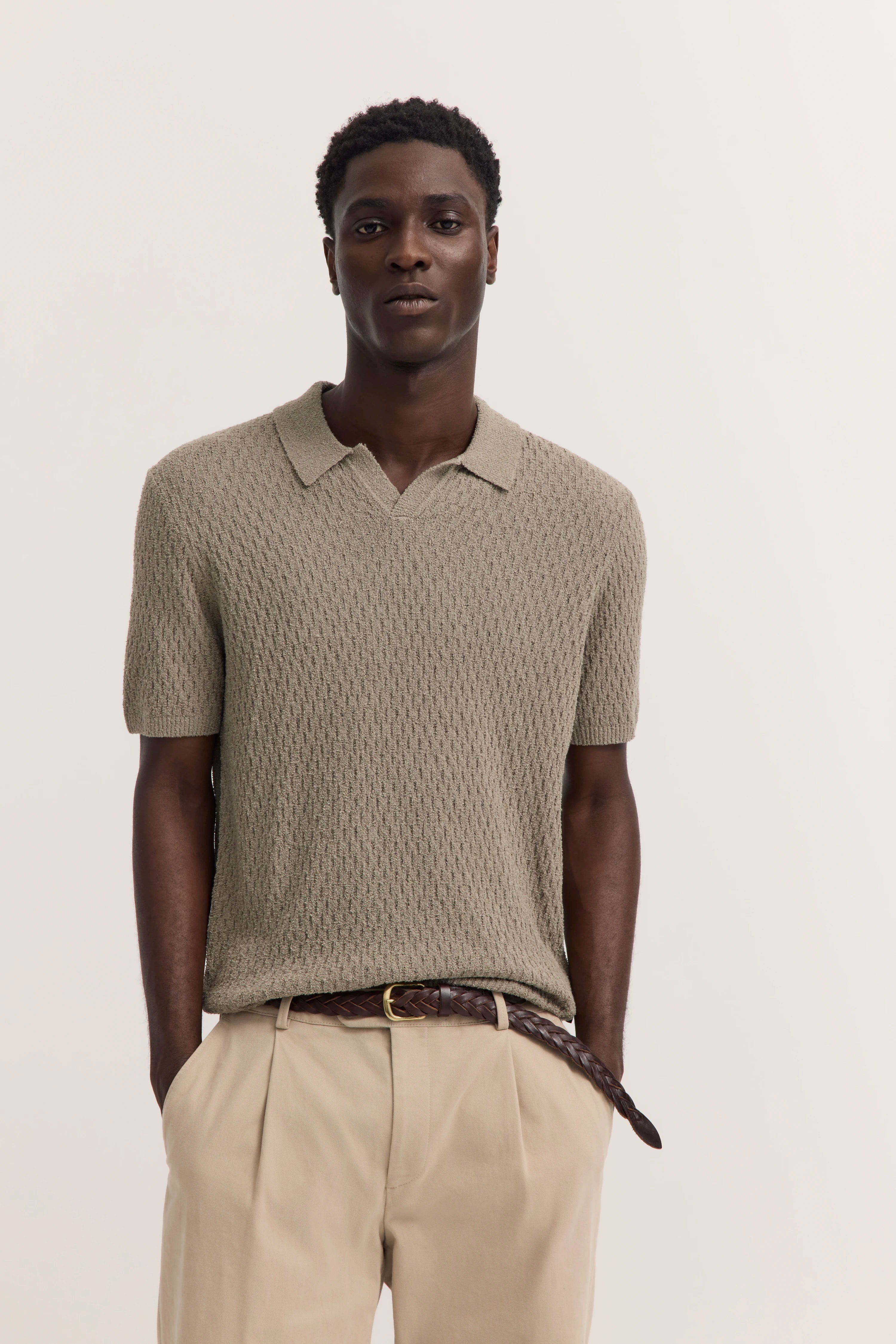 bugatti Modelbild, entspanntes Posing, olivgrünes Strickpolo, beige Hose, brauner Gürtel.