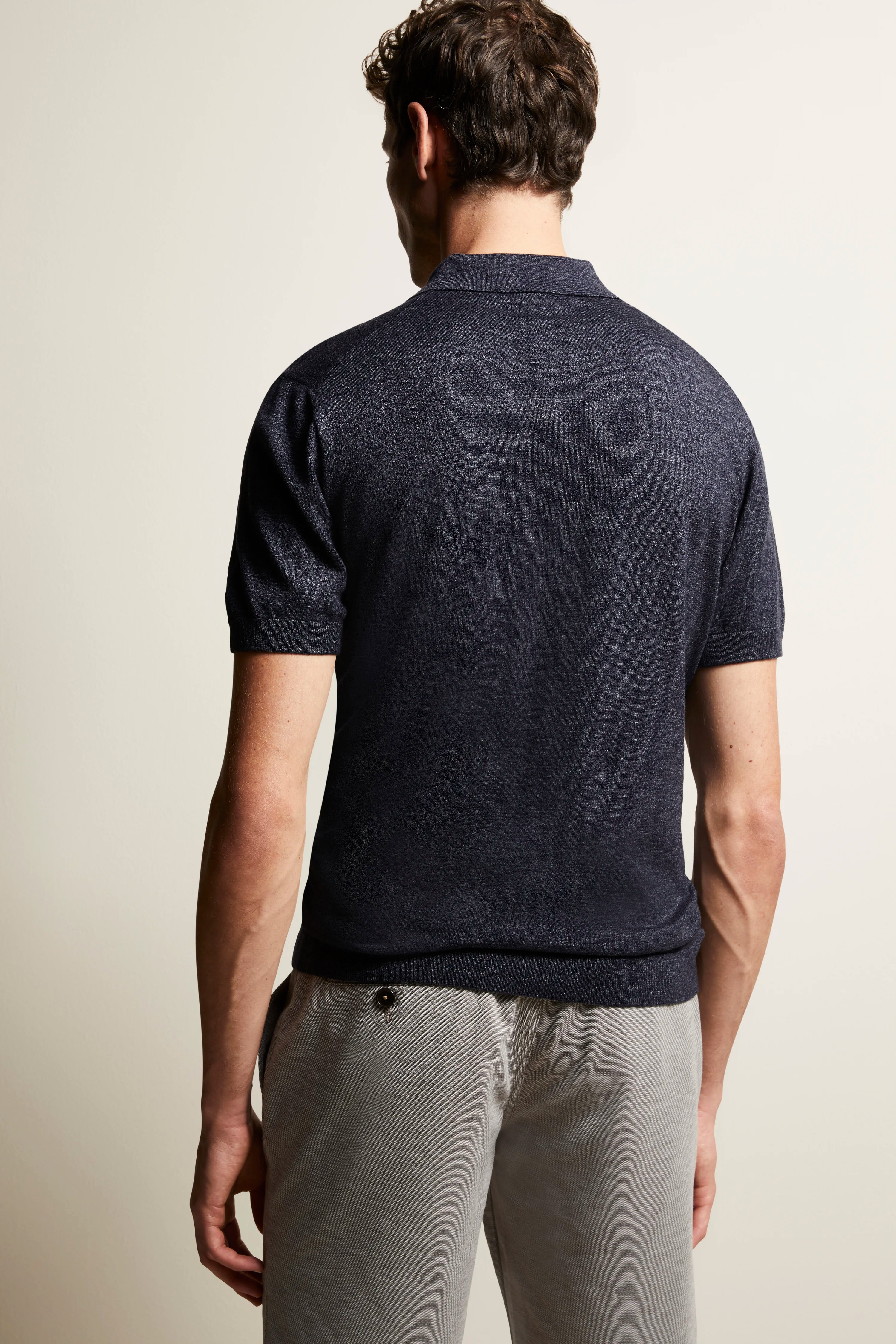 Navy polo shirt and gray joggers in casual model photo from the back.