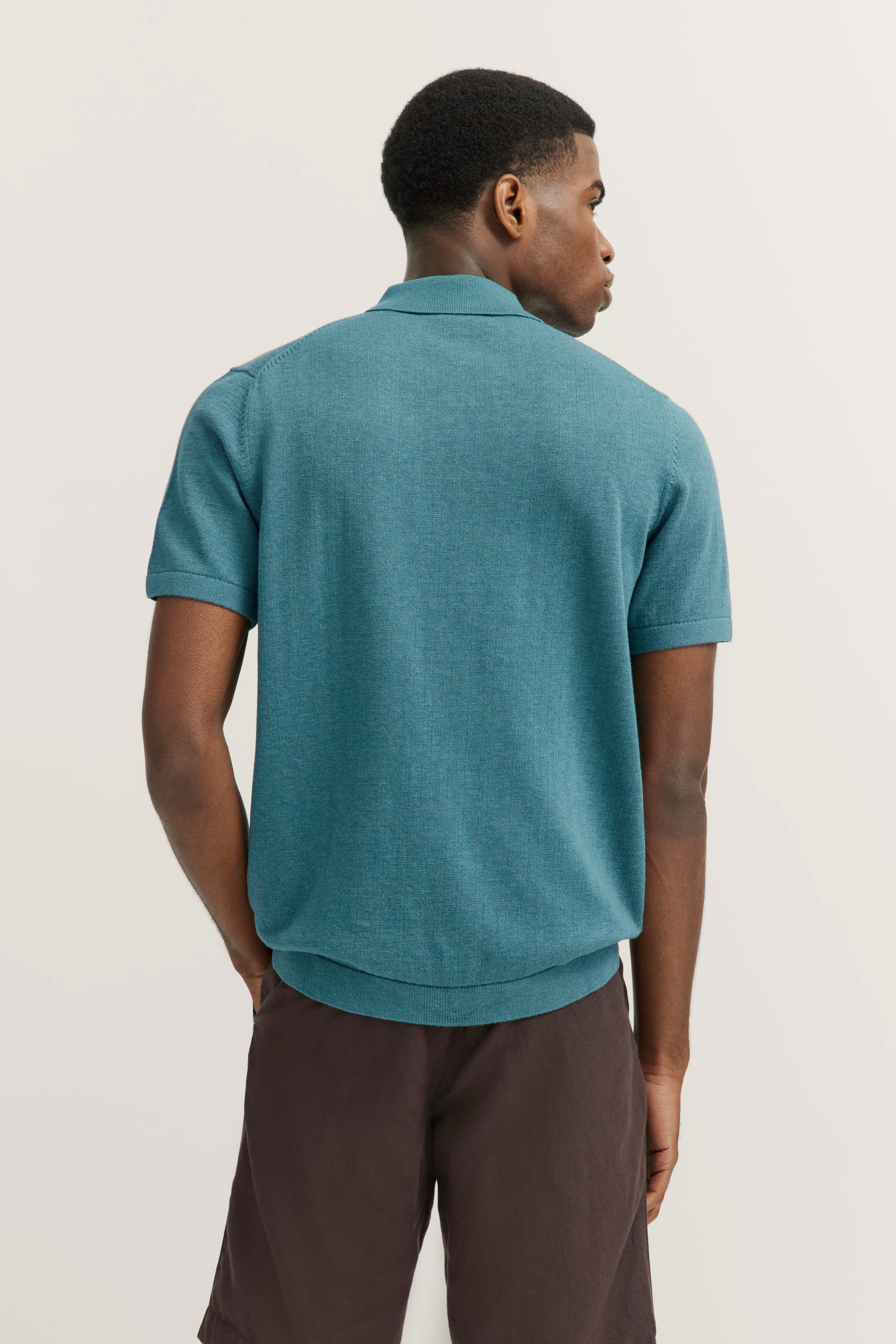 Model in turquoise bugatti polo shirt and brown shorts, back view, relaxed pose.