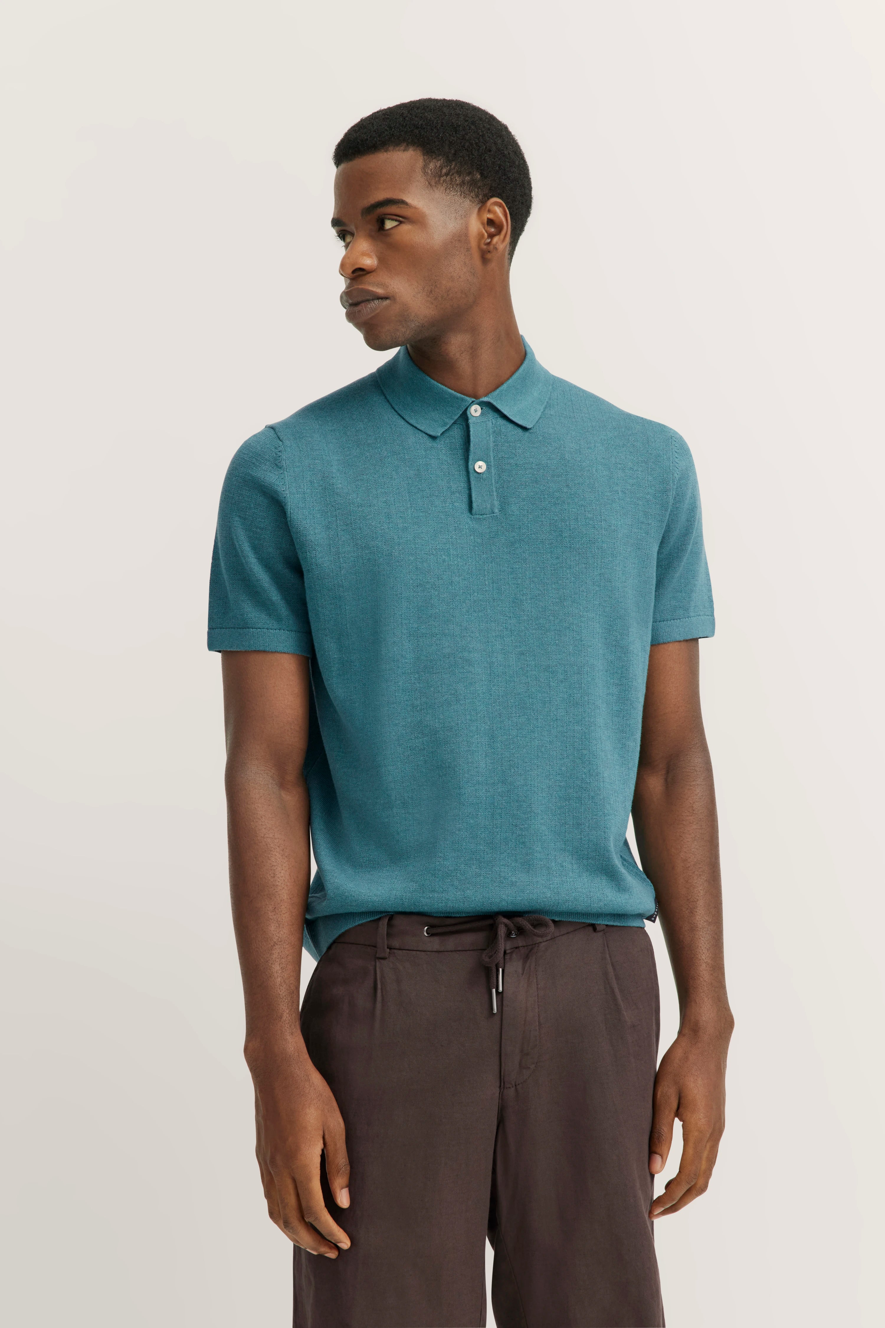 Model in turquoise polo shirt and brown pants by bugatti, casual pose.