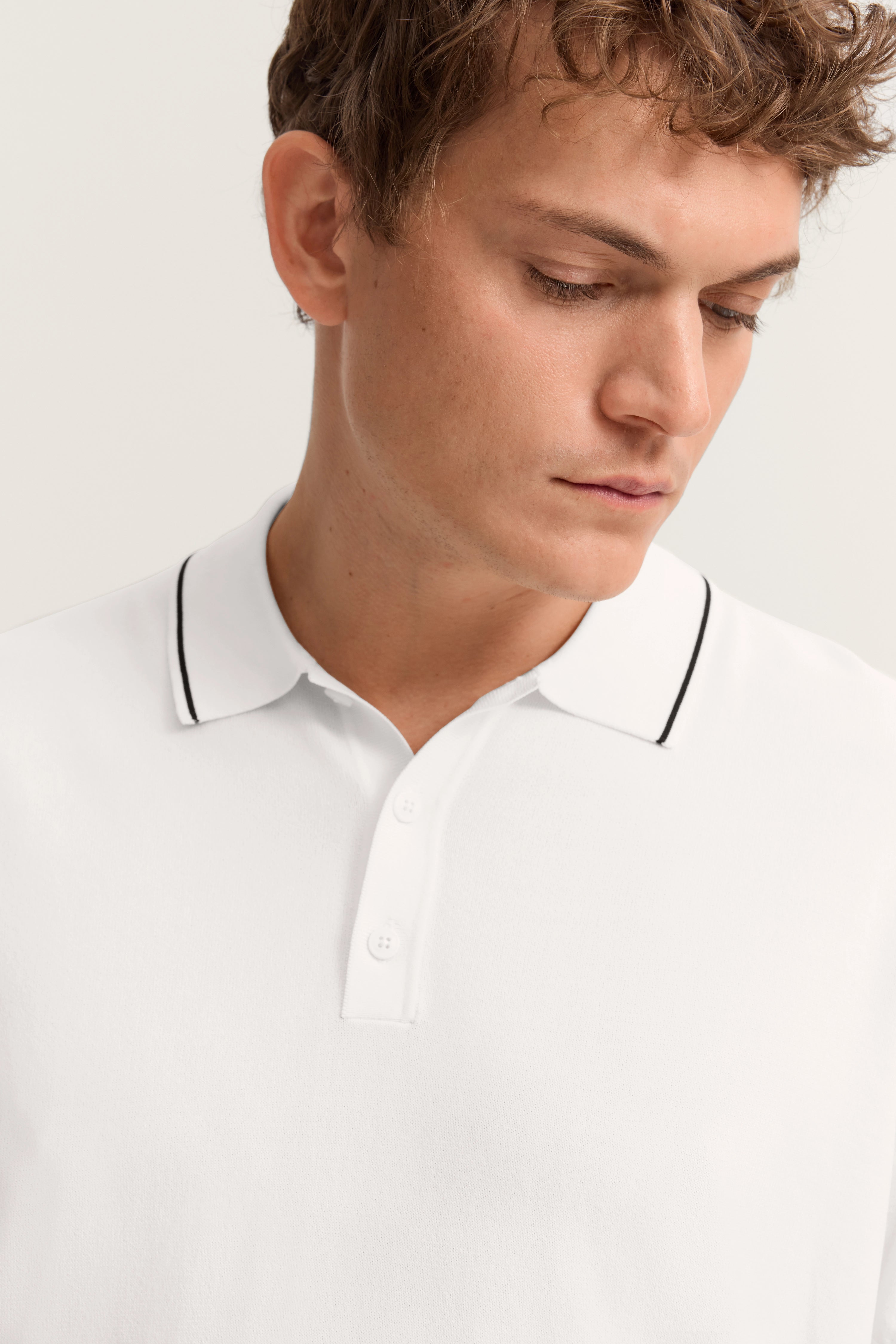 Weißes bugatti Polohemd mit schwarzem Kragenrand, Modelbild zeigt entspanntes Posing.