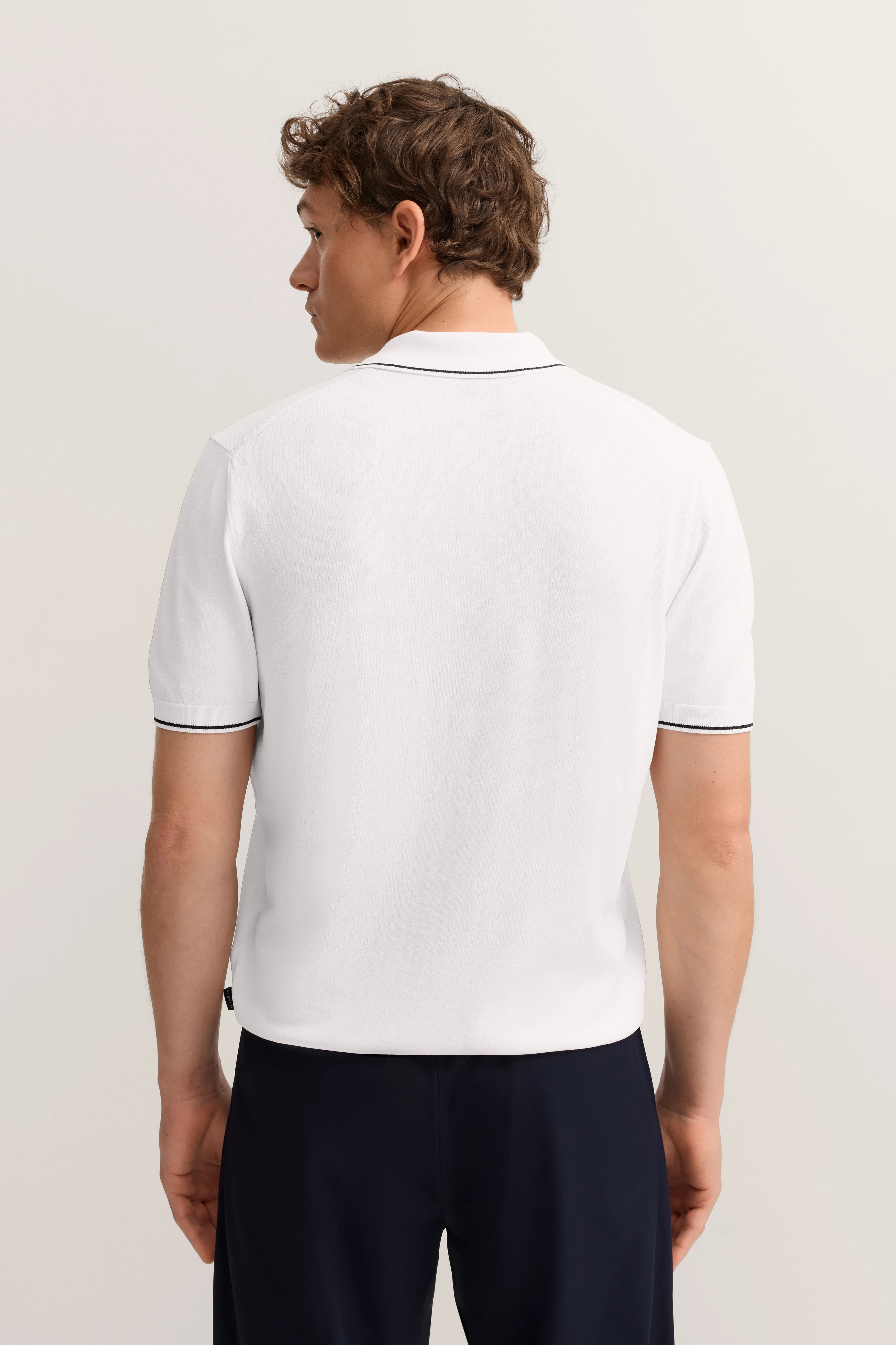 Weiße bugatti Polo-Shirt Rückansicht, schwarzer Kragenrand, getragen von Model, entspannte Haltung.