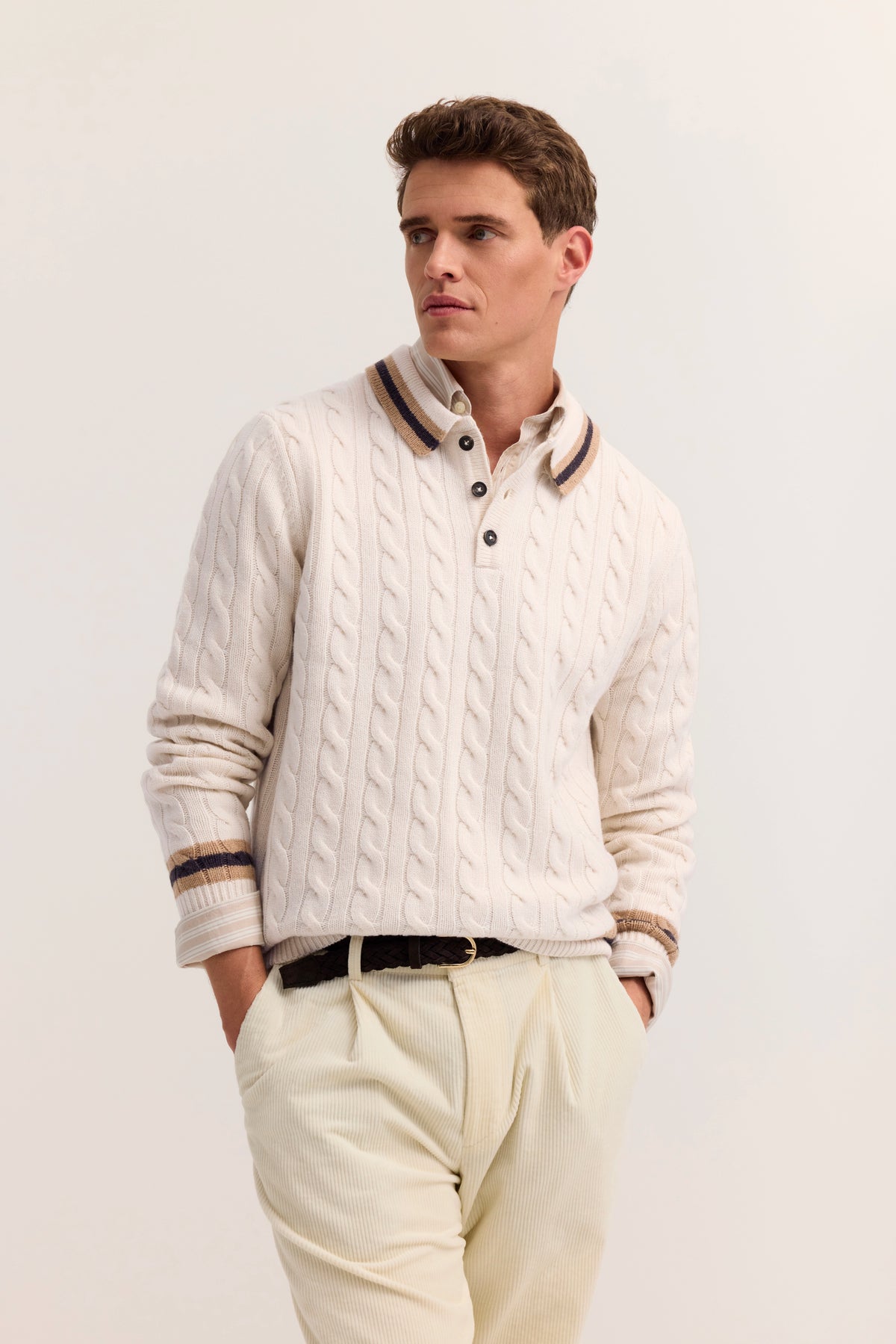 Model in cremefarbenem Zopfstrickpullover mit gestreiftem Kragen, lässig posierend.
