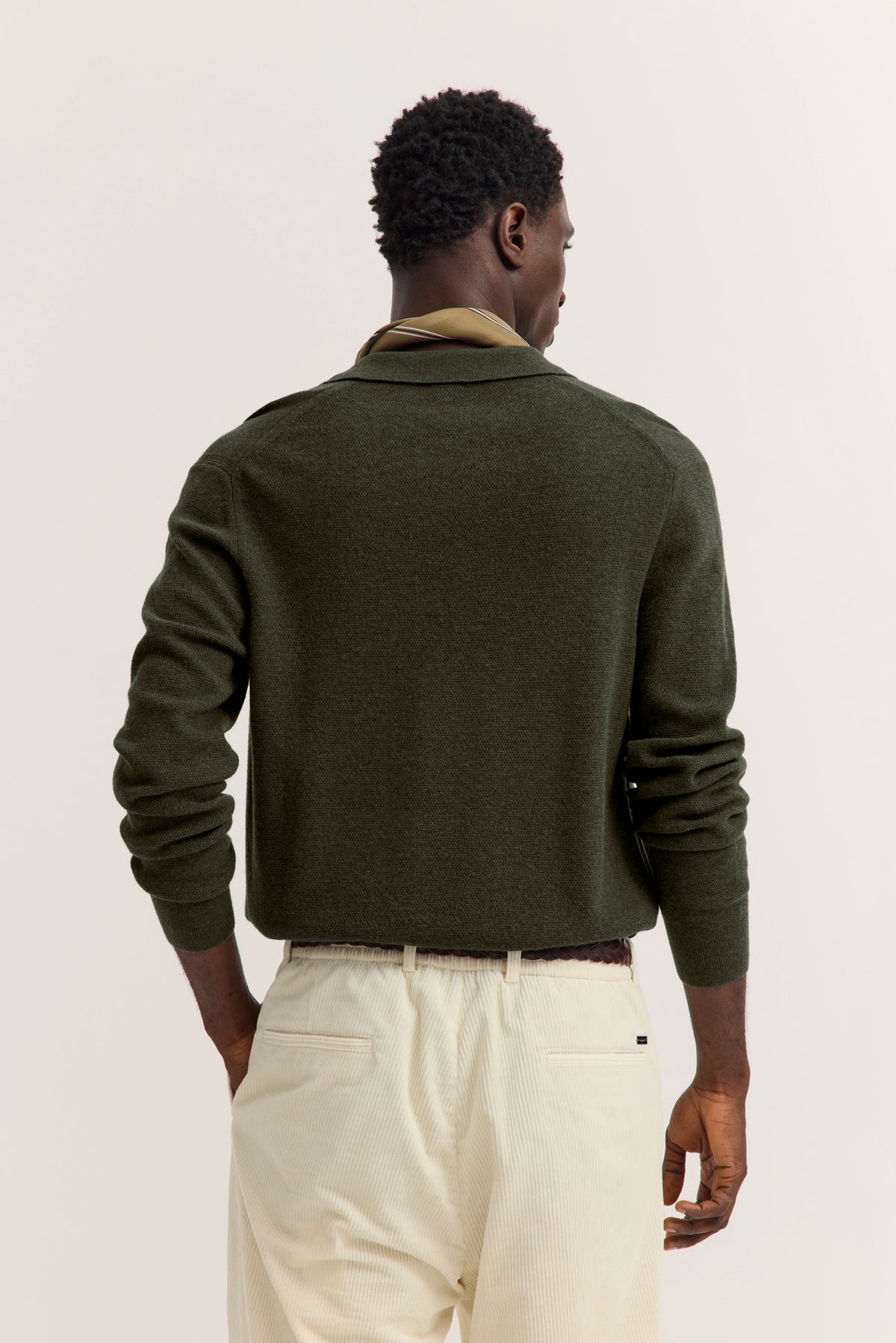 Grüner bugatti Pullover, beige Hose, Rückansicht Modelbild, entspannte Pose.