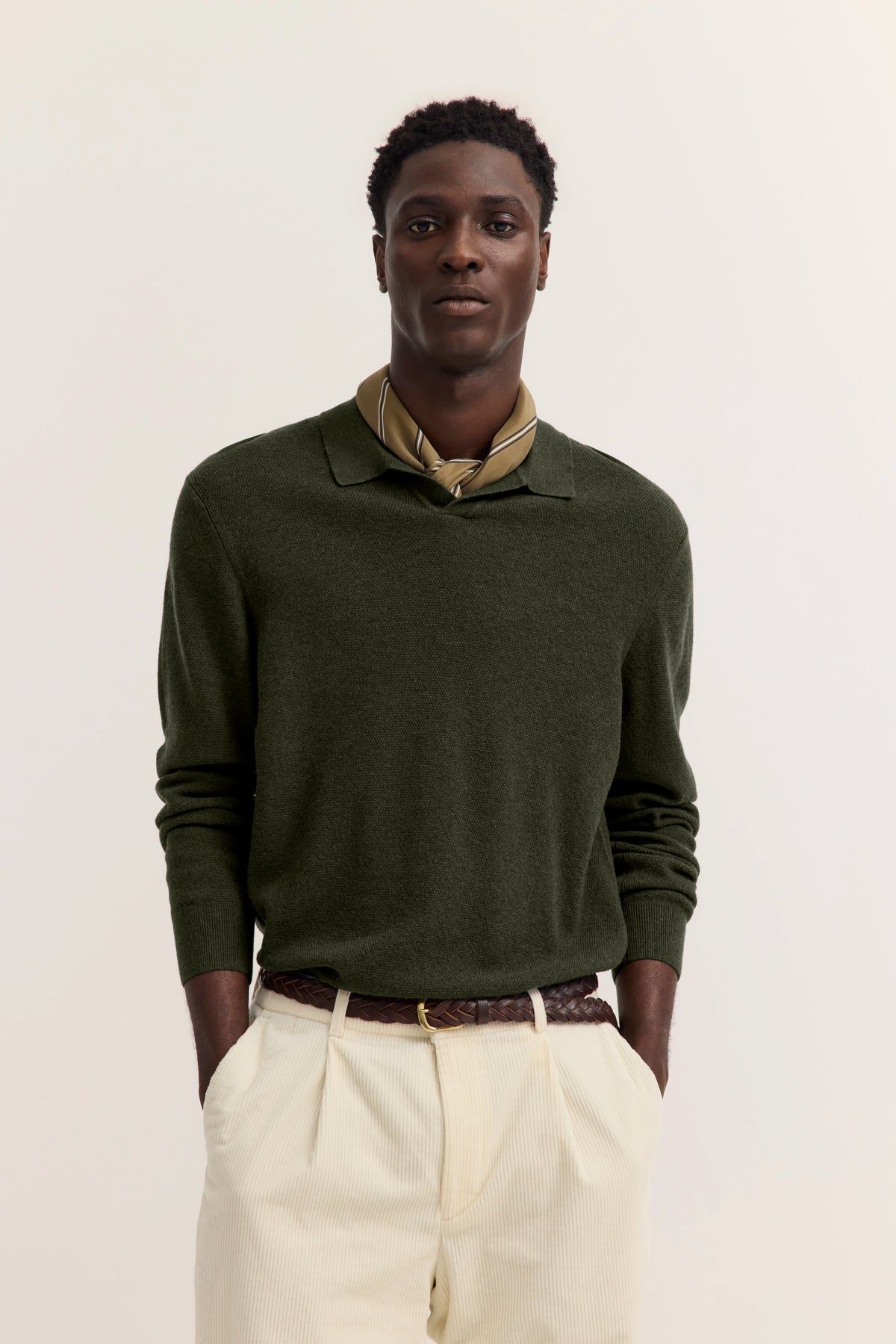 Dunkelgrüner Pullover und cremefarbene Hose, Modelbild, lässige Pose.