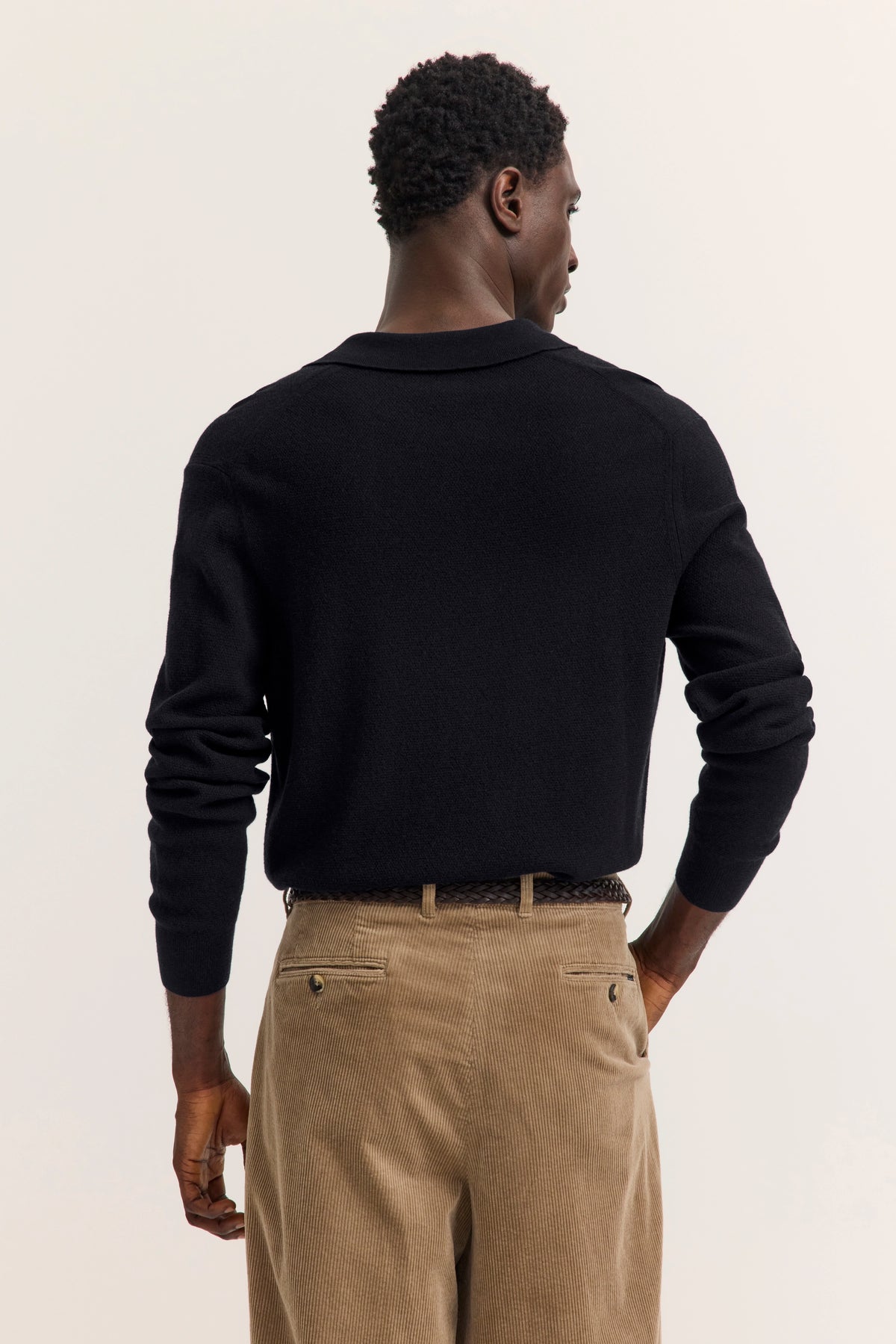 Schwarzer bugatti Pullover, beige Cordhose, Model von hinten, entspannte Pose.