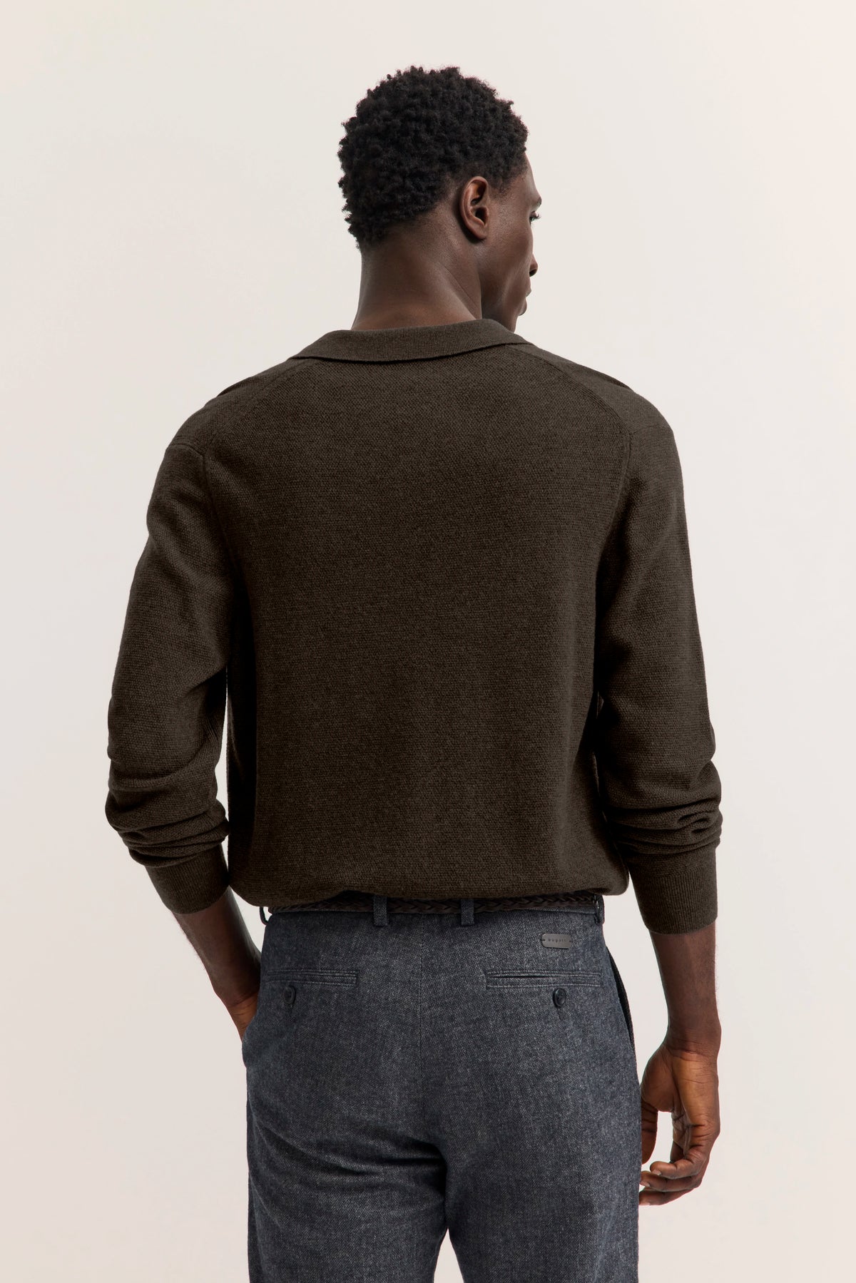 Bugatti Model in braunem Pullover, graue Hose, Rückansicht, entspanntes Posing.