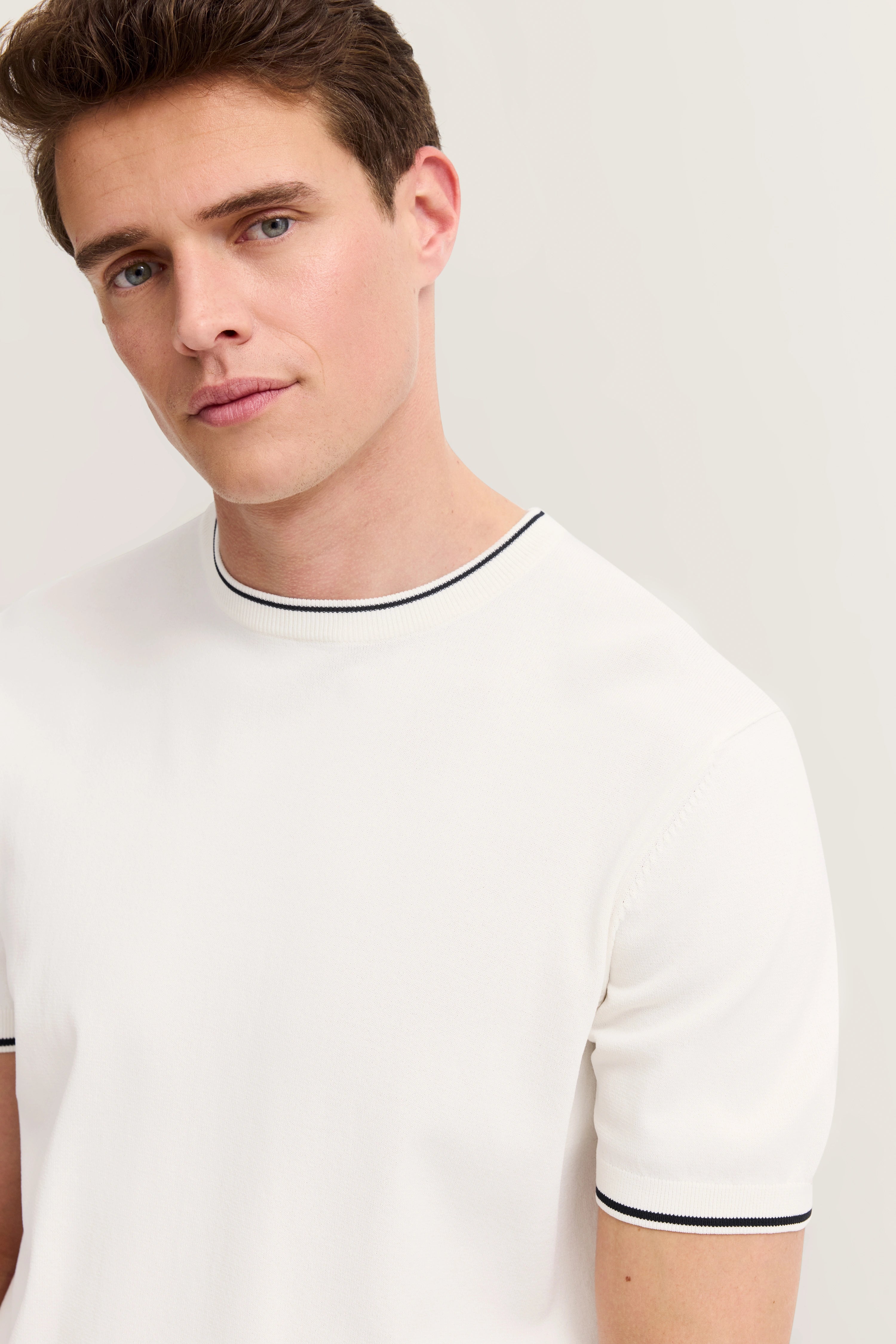 White T-shirt with black collar trim, model with neutral expression.