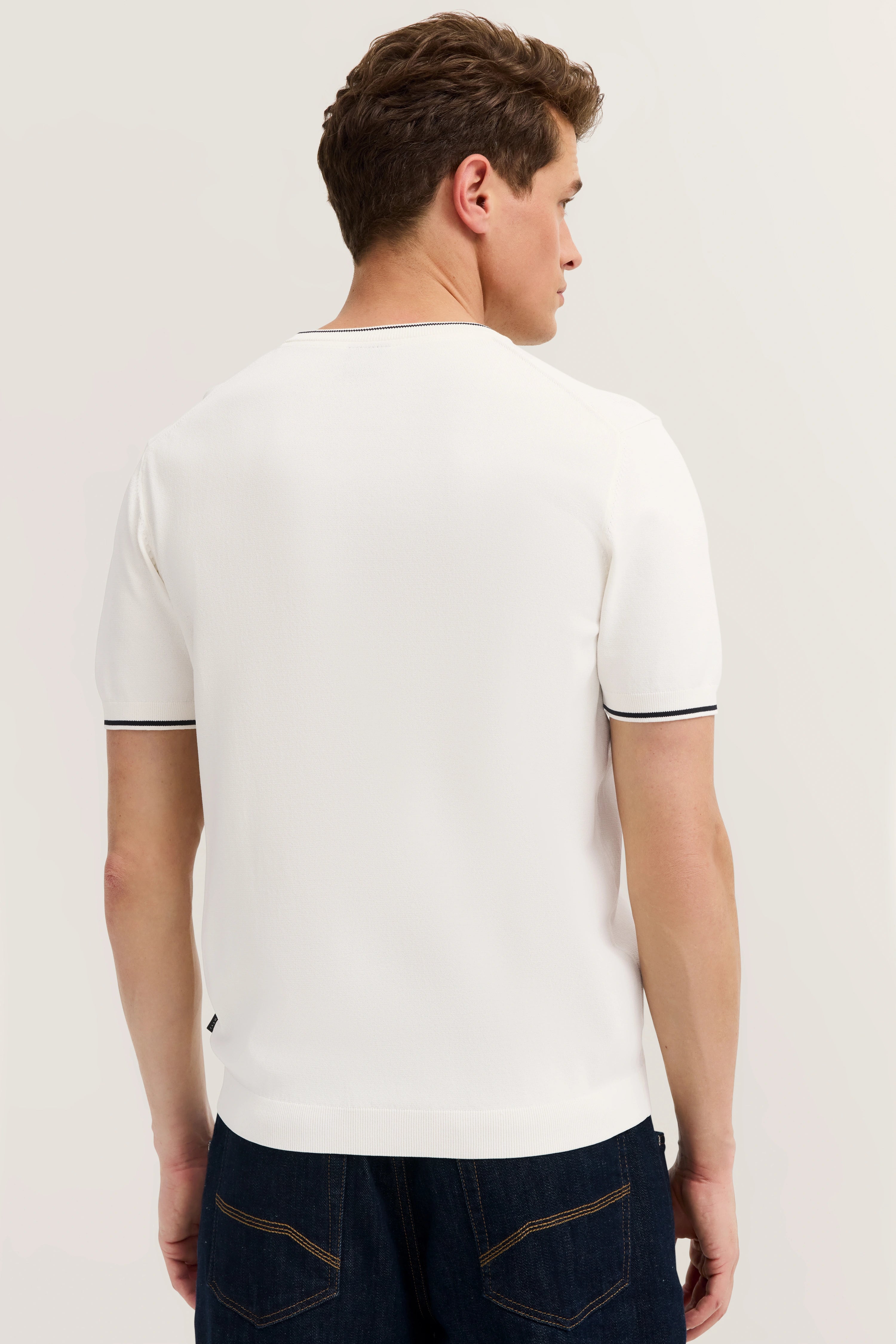 White bugatti T-shirt, back view, casually paired with dark jeans, model from behind.