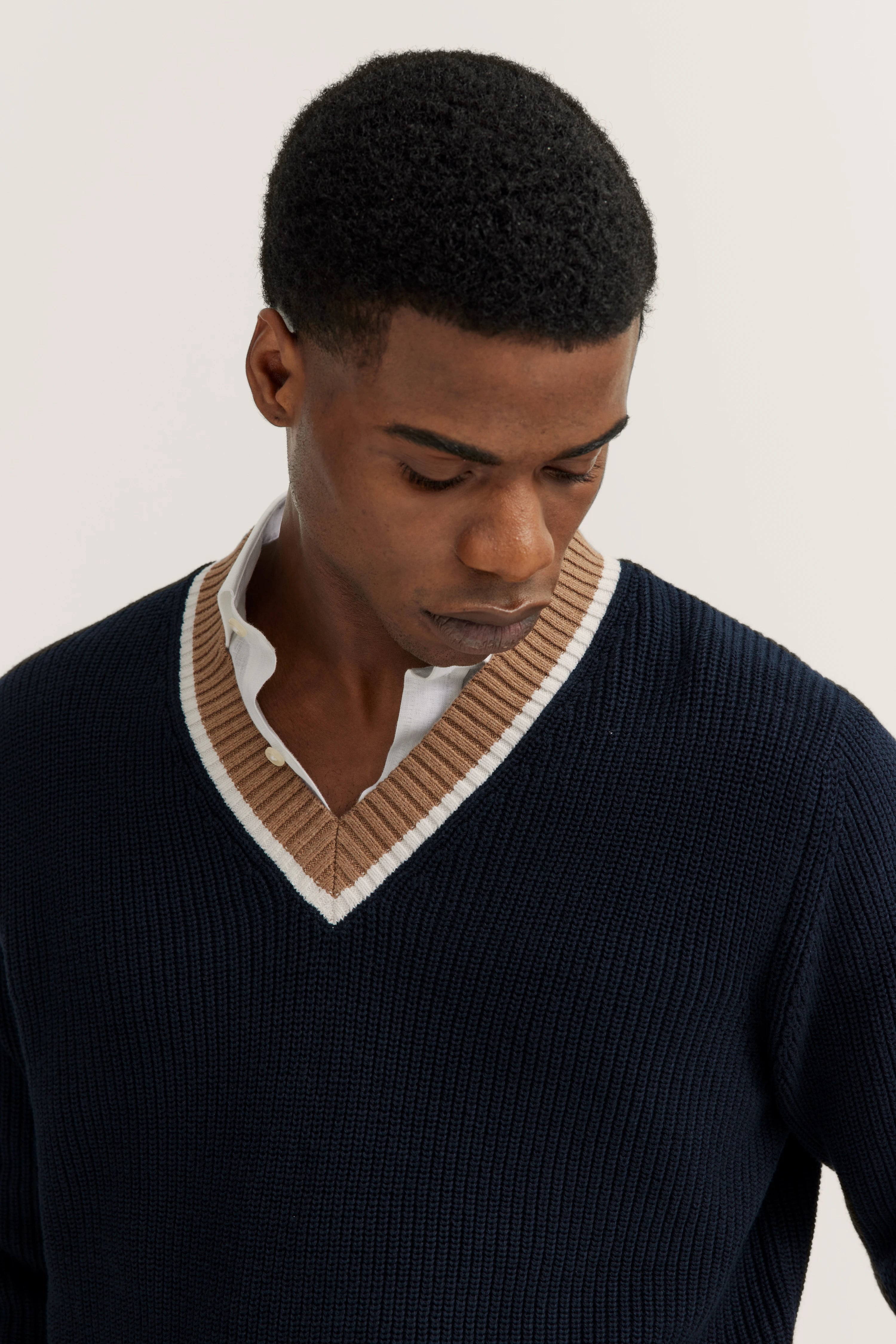 Navy V-Pullover mit beigem, gestreiftem Kragen, Modelbild, entspannter Blick nach unten.