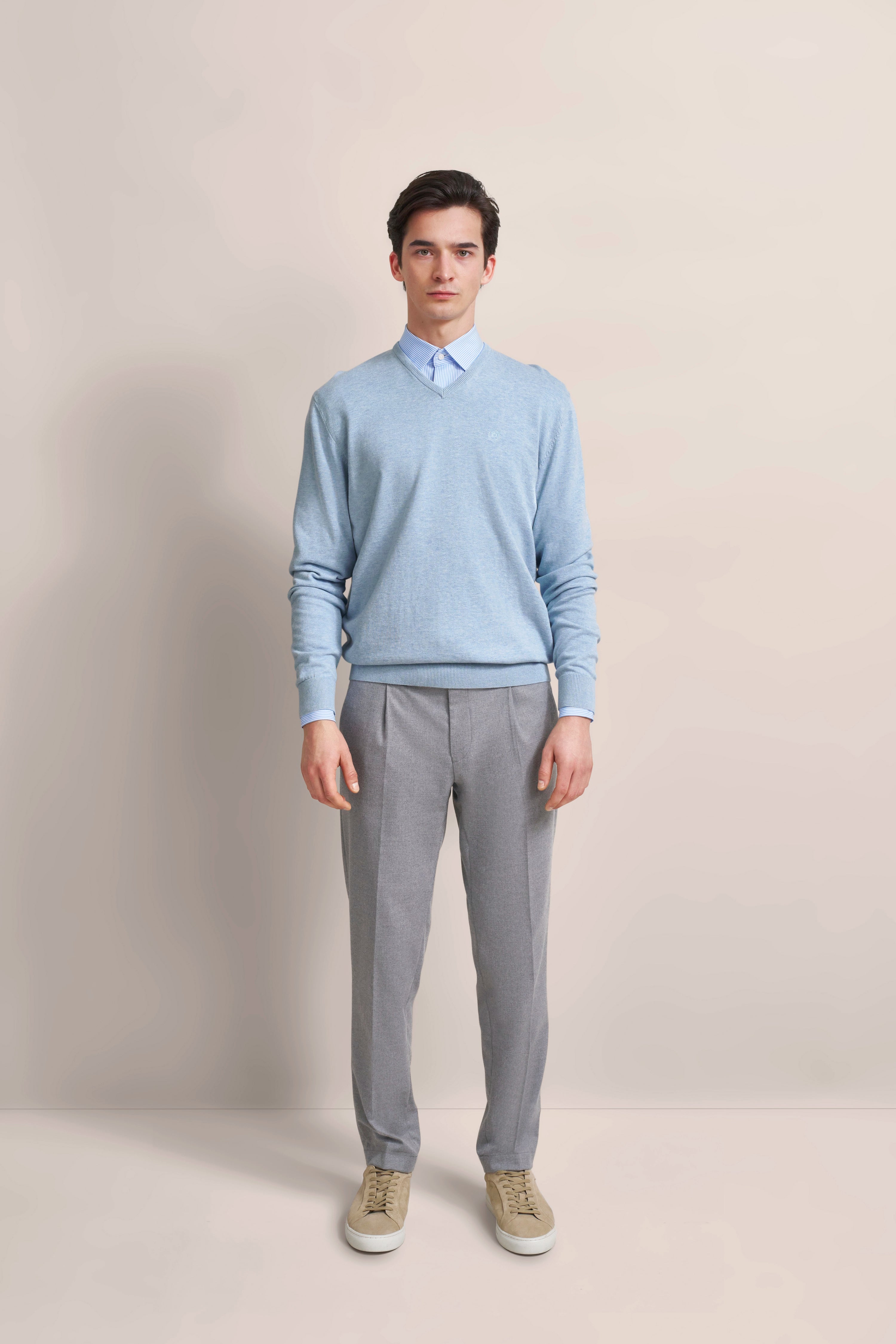 Model in hellblauem Pullover, blauer Hemdkragen, graue Hose. Lockeres Posing. bugatti Stil.