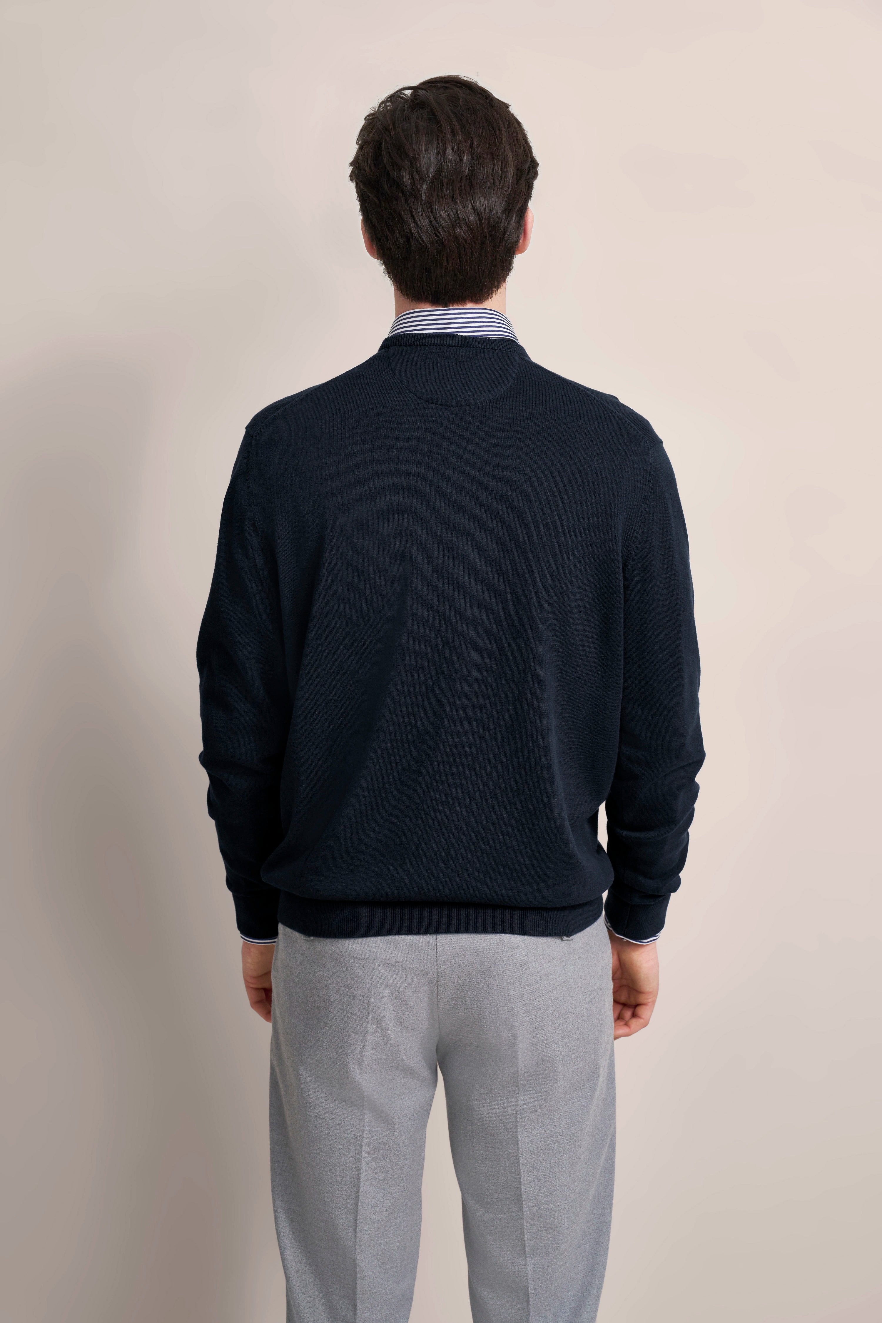 Model in dunkelblauem Pullover und grauer Hose von bugatti, Rückansicht.