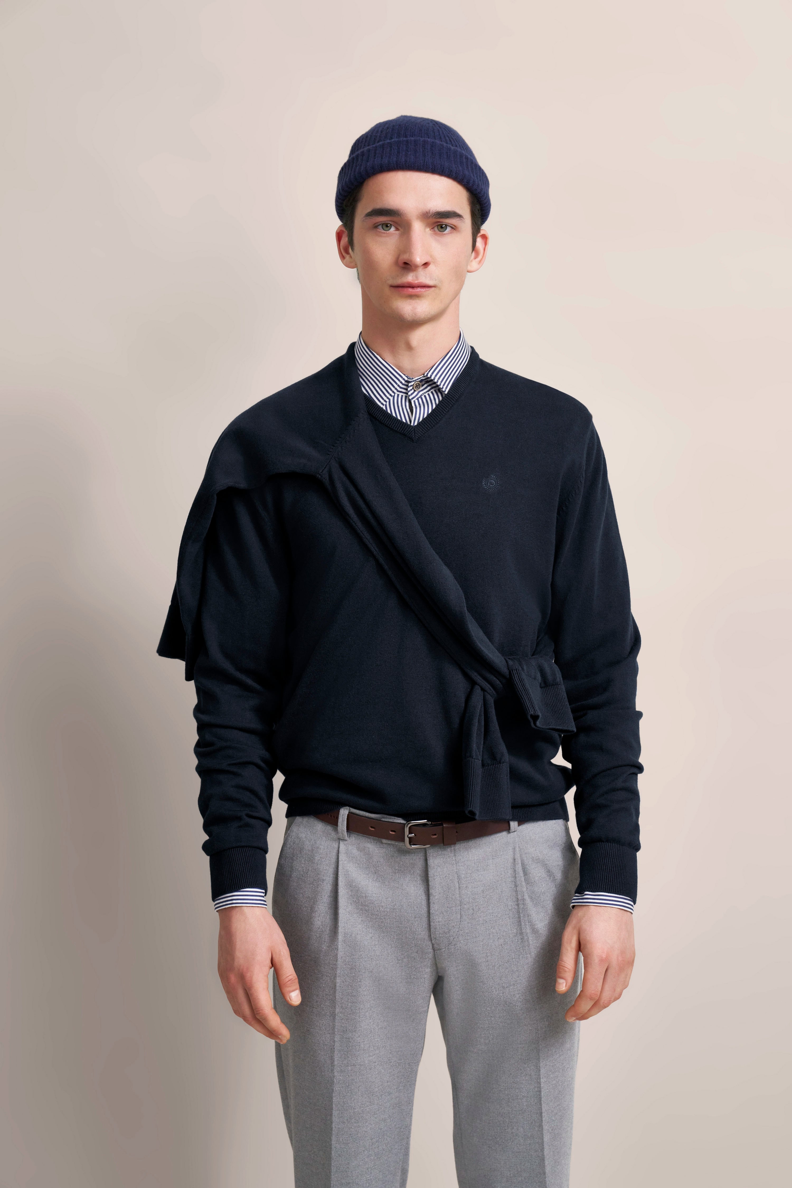 Modell im bugatti-Look: Dunkelblauer Pullover, gestreiftes Hemd, graue Hose, entspannte Pose.