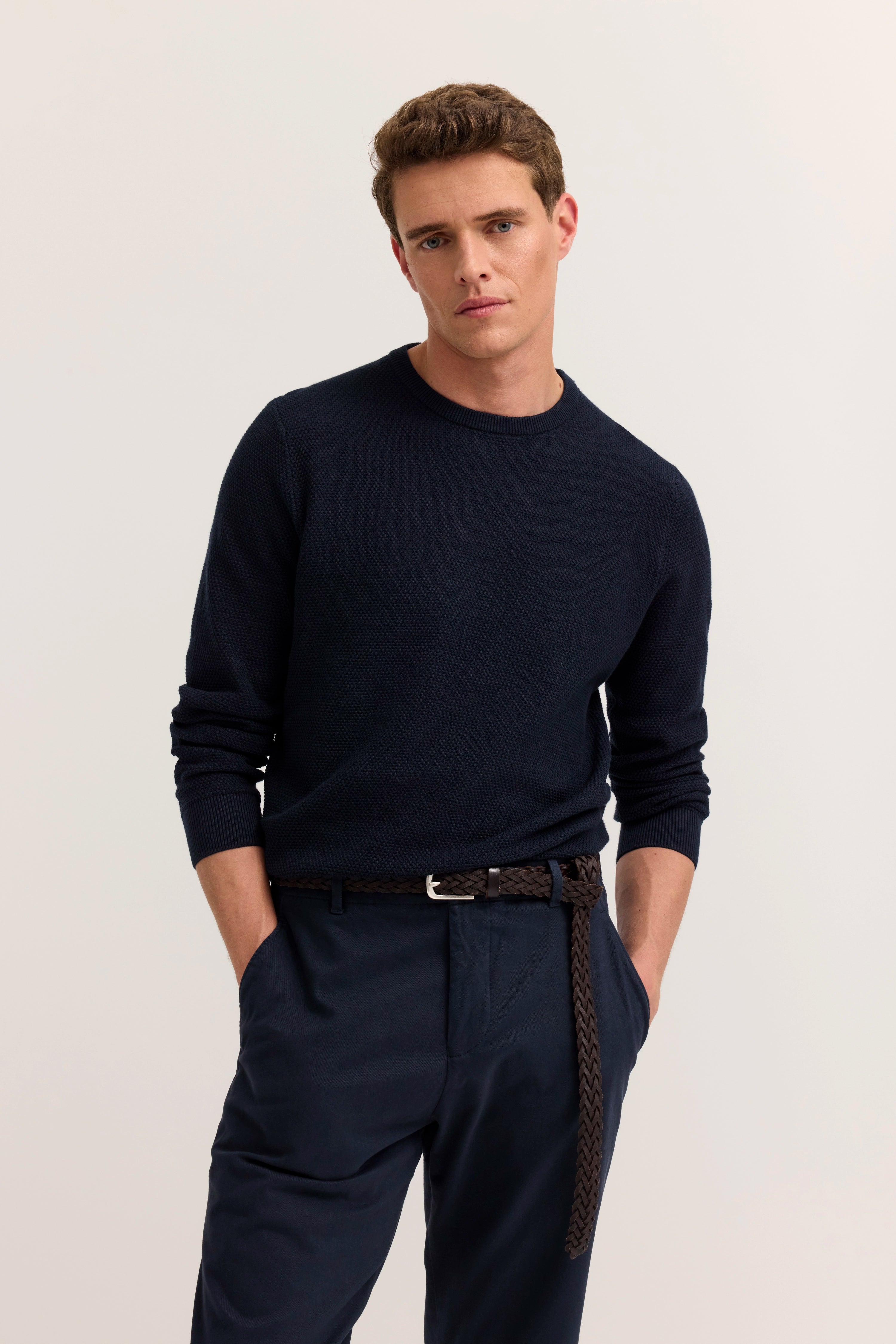 Model in marineblauem Pullover und Hose, leger posierend, Hände in den Taschen.