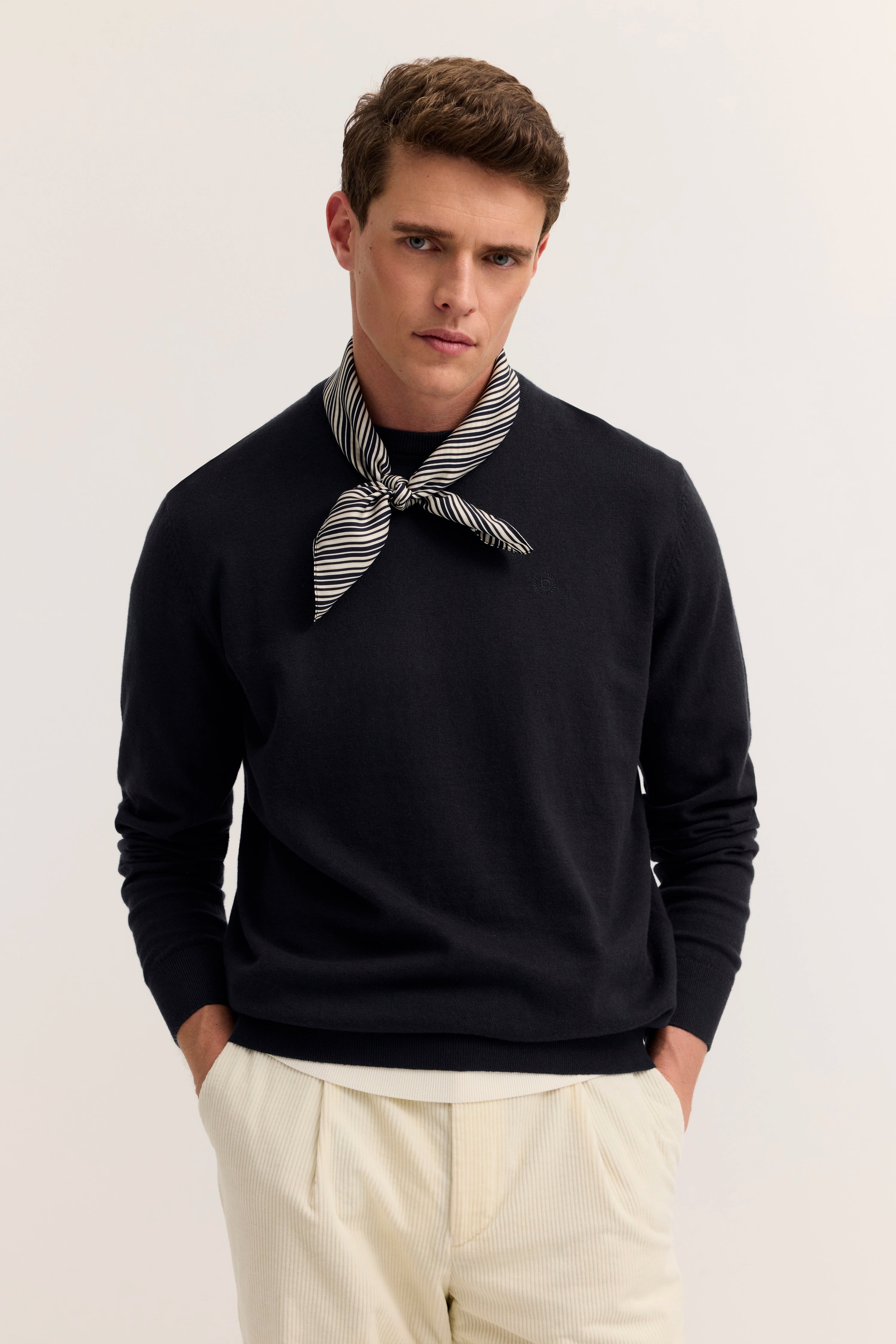 Model mit schwarzem Pullover, gestreiftem Schal, cremefarbener Hose