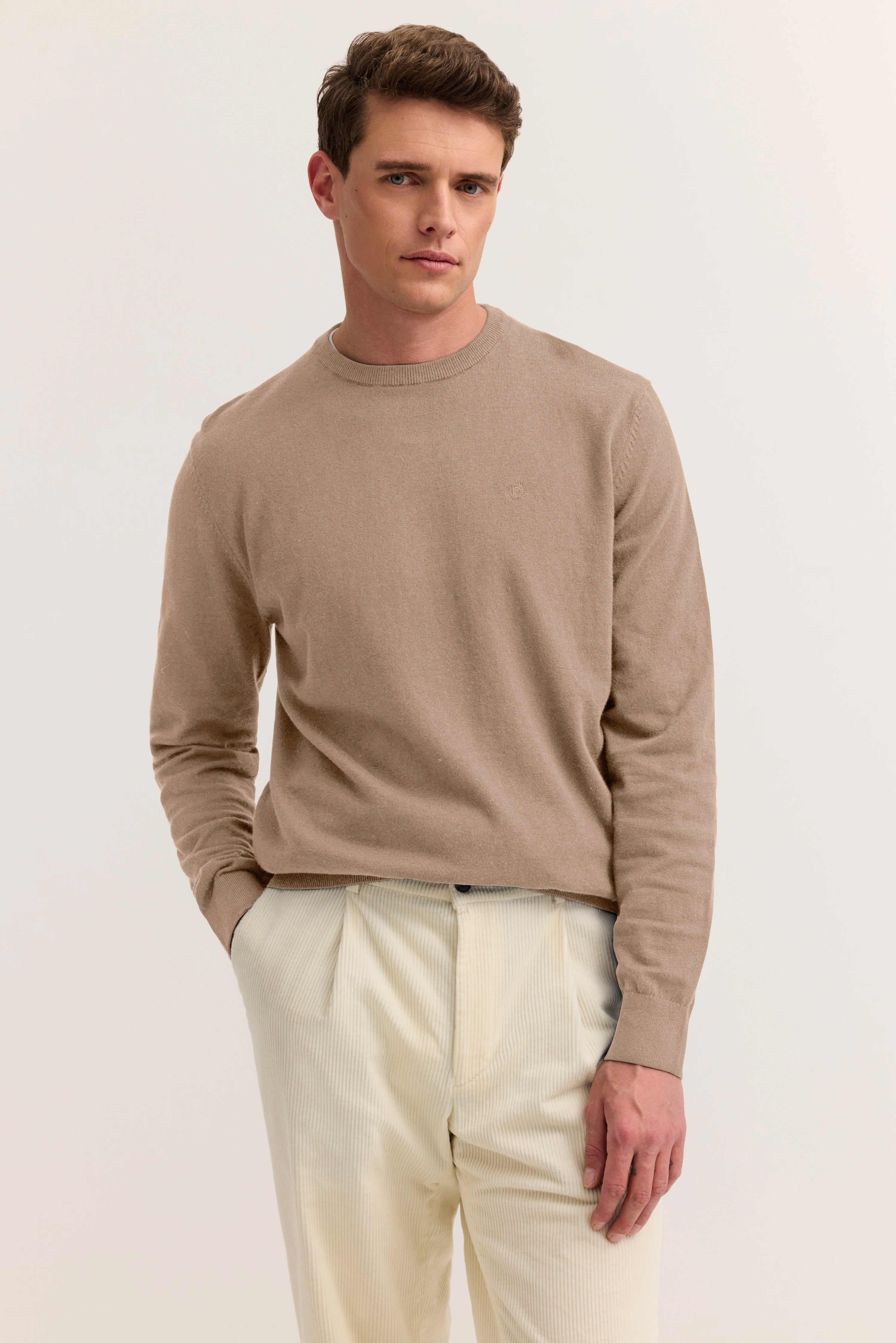 Beiges Langarmshirt und cremefarbene Hose, Model stehend, Hände in Taschen.