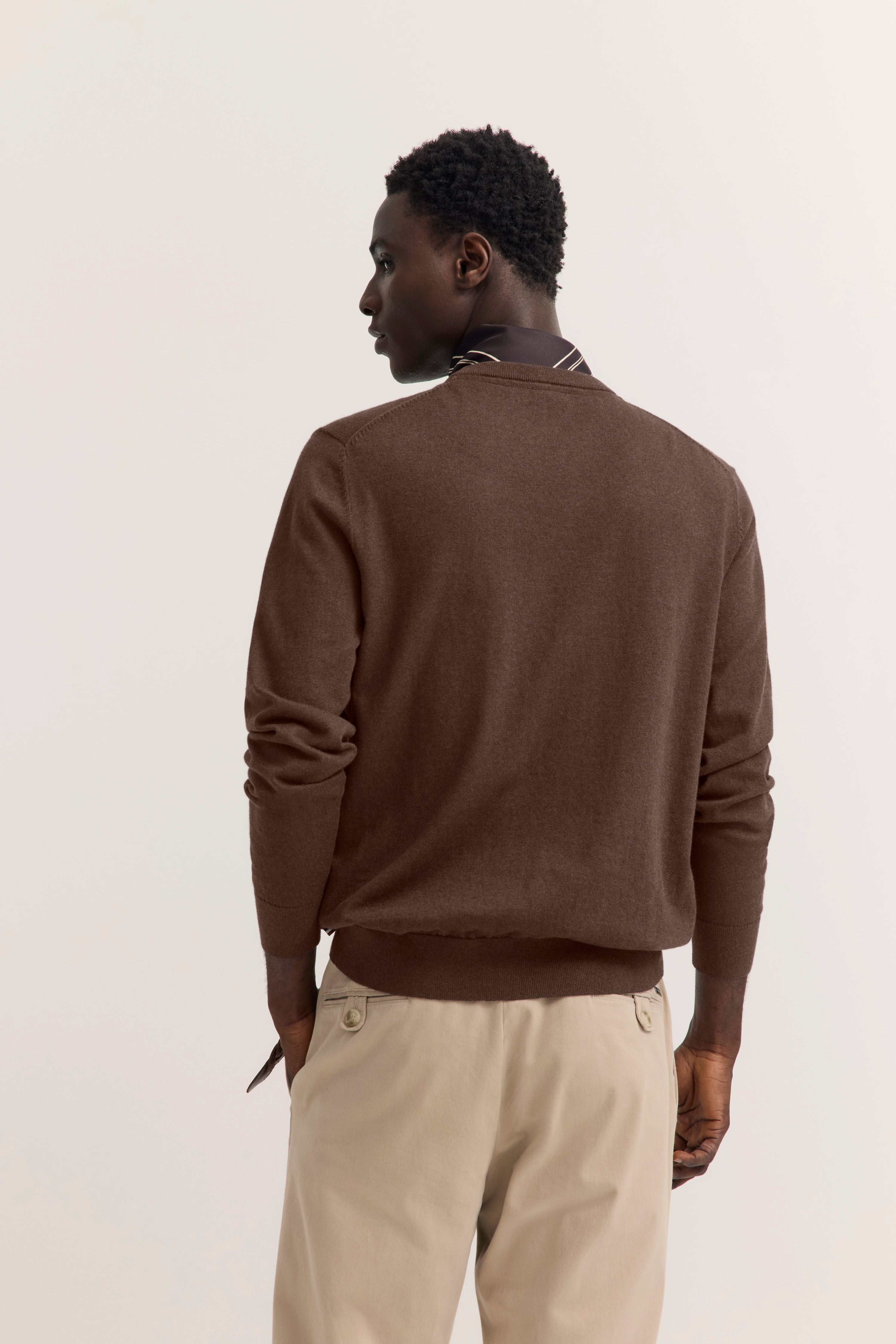 Brauner Pullover von bugatti mit beigen Hosen, Model seitlich stehend, lässig-elegante Ausstrahlung.