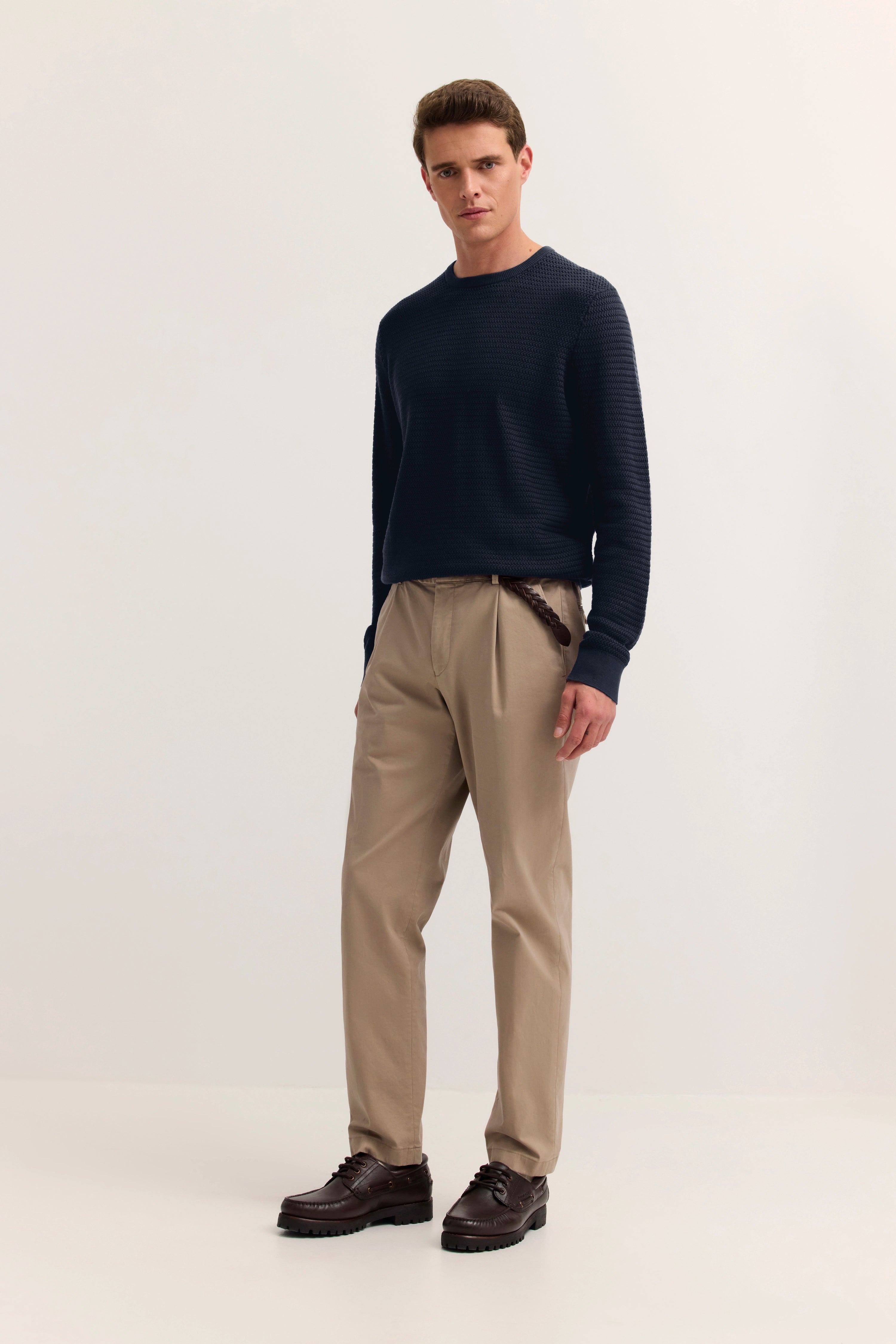 Model mit dunkelblauem Pullover, beige Chinos, braunen Schuhen