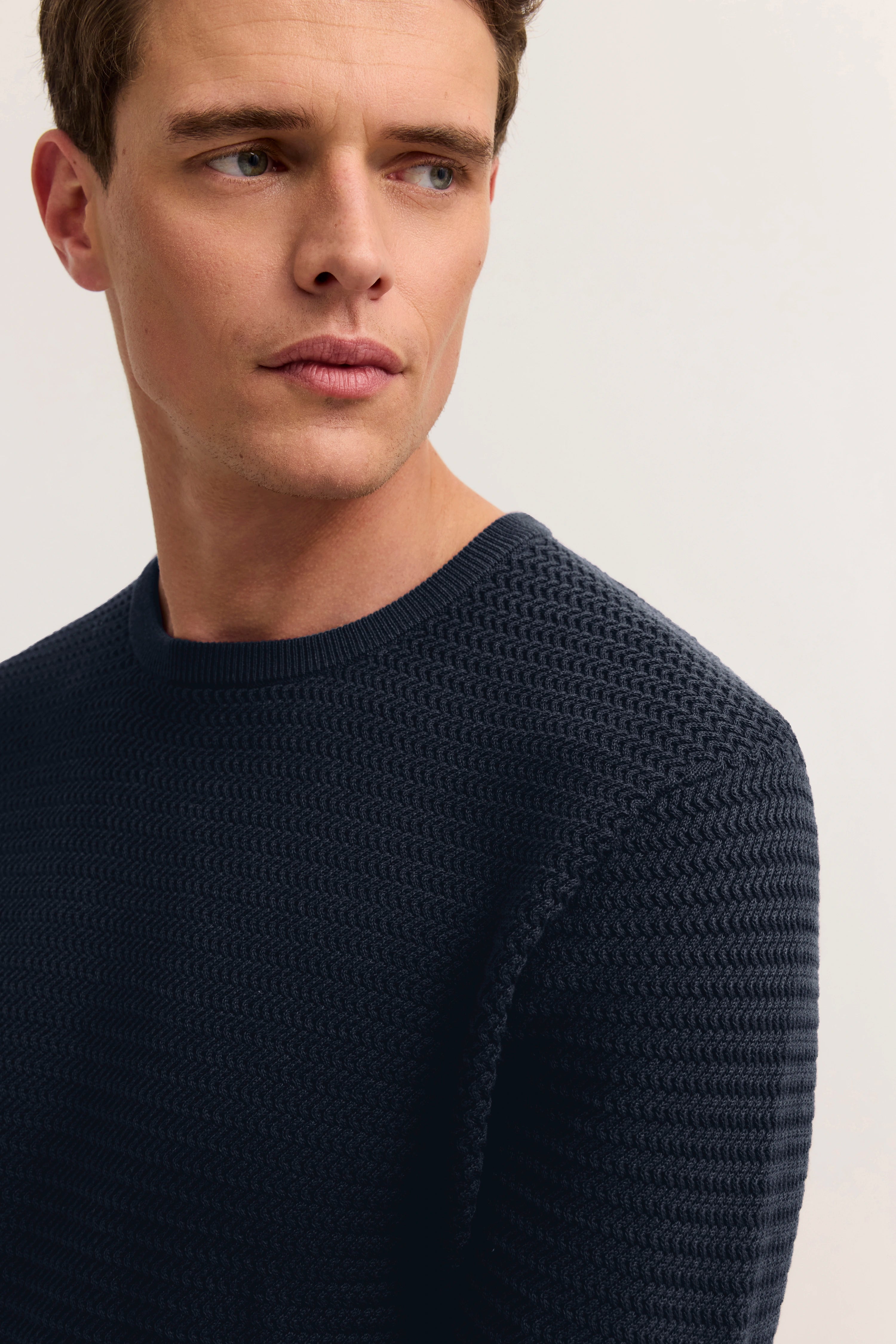 Model in marineblauem, strukturiertem bugatti-Pullover, seitliches Posing.