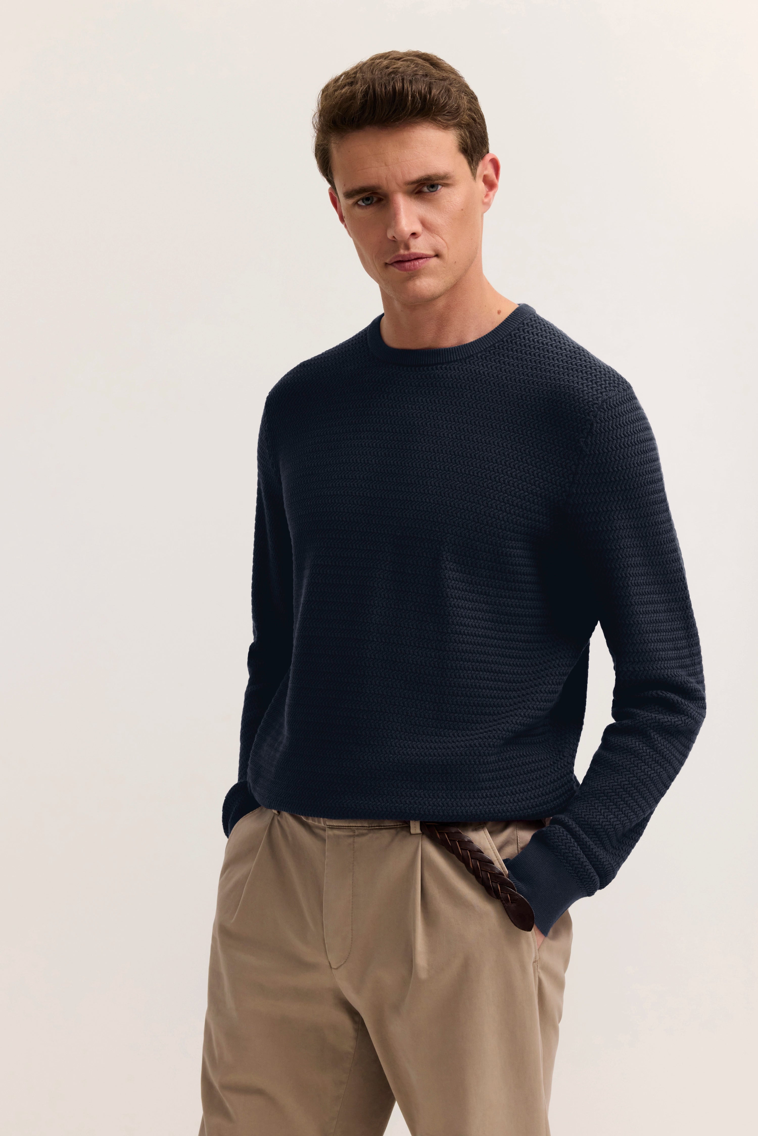 bugatti Outfit: Dunkelblauer Pullover, beige Hose, legeres Modelbild, lässige Pose mit Händen in den Taschen.