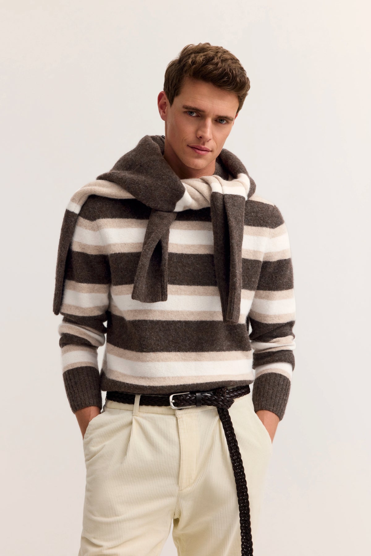"bugatti Modelbild: Mann in gestreiftem Pullover in Braun und Beige, legeres Posing mit Händen in Taschen."