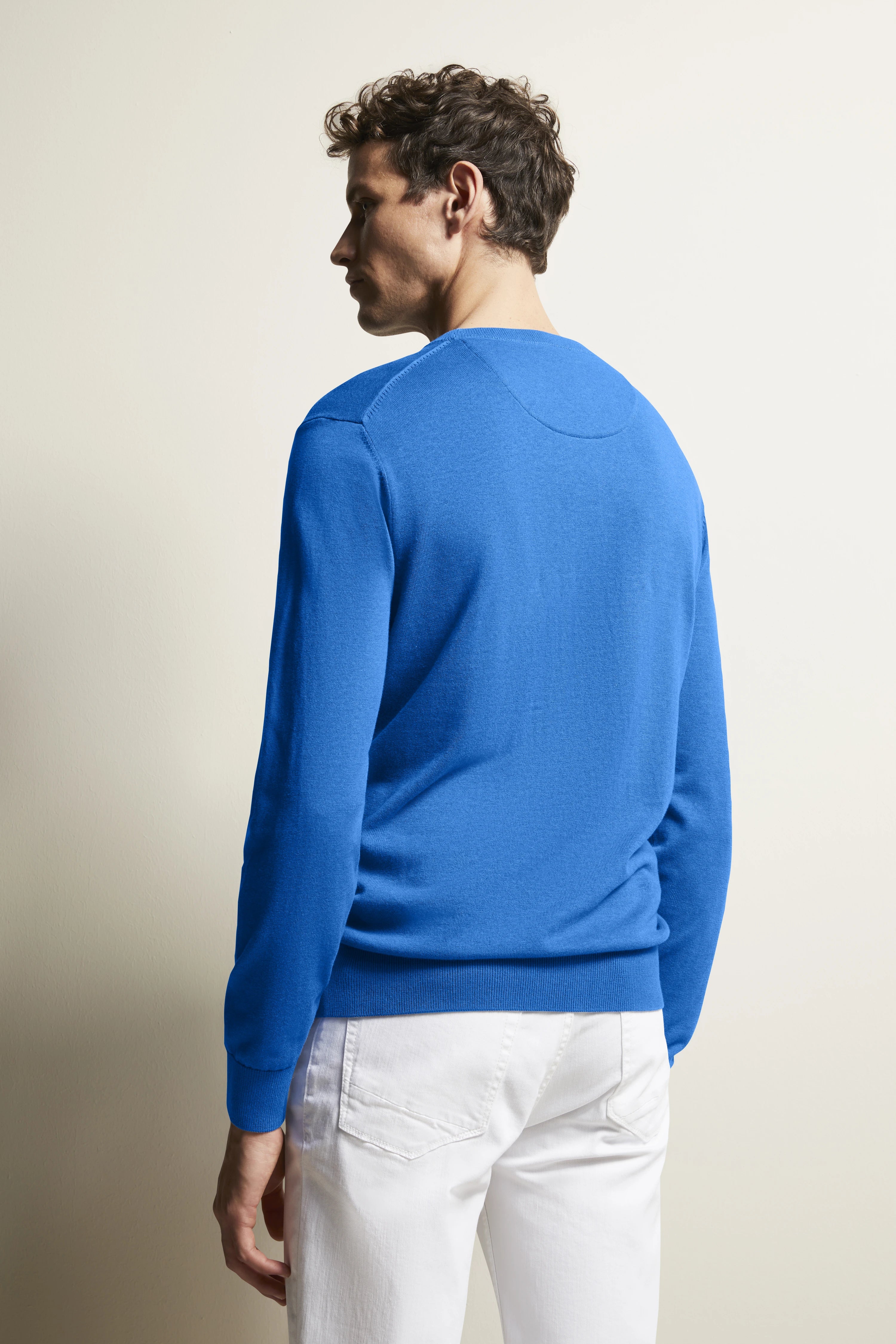 Blauer bugatti Pullover, weißer Hose, Model von hinten, entspannte Pose.