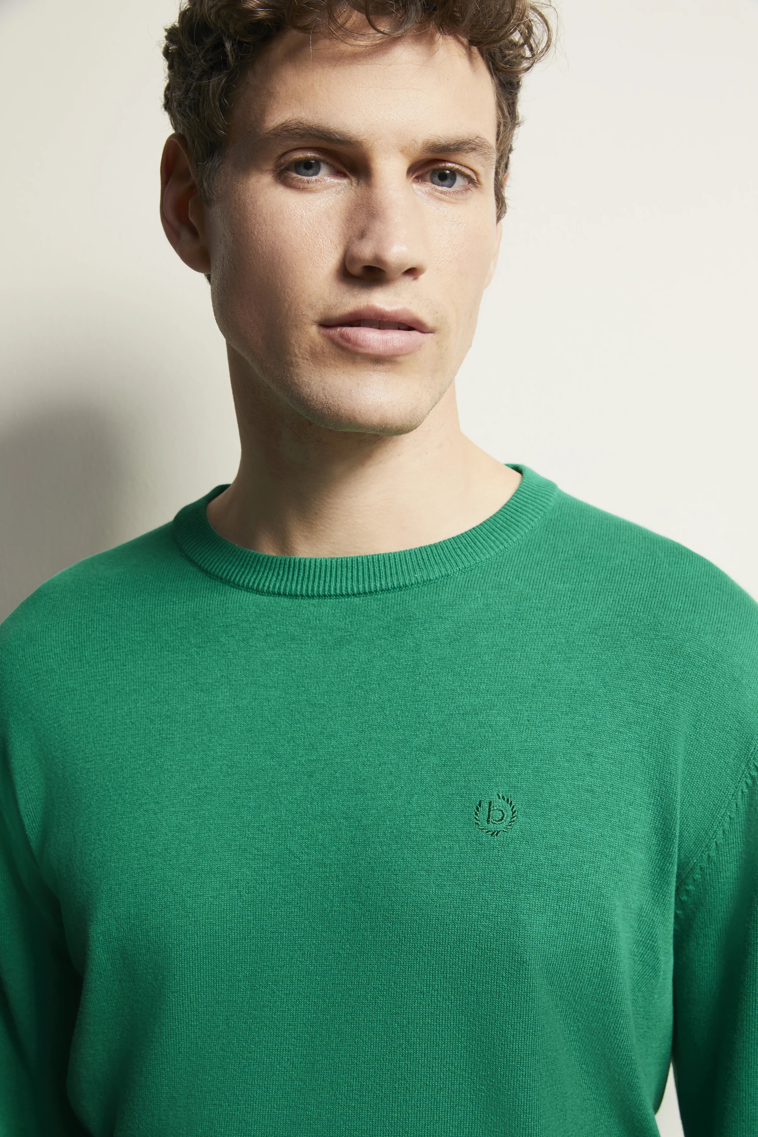 Model in grünem bugatti Pullover, legeres Posing, Halbprofilansicht.