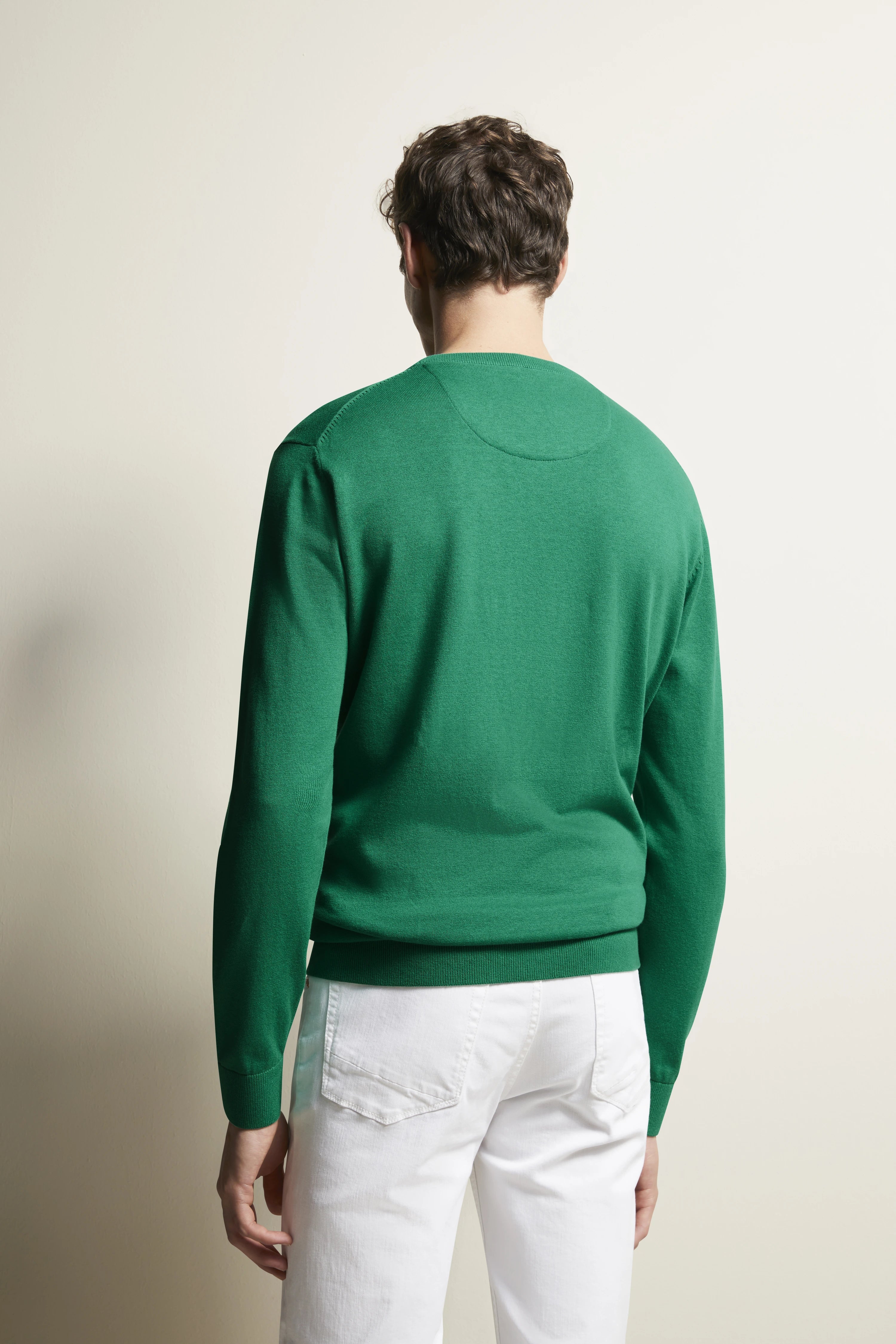 Grüner bugatti Pullover und weiße Hose, Model von hinten, legeres Posing.