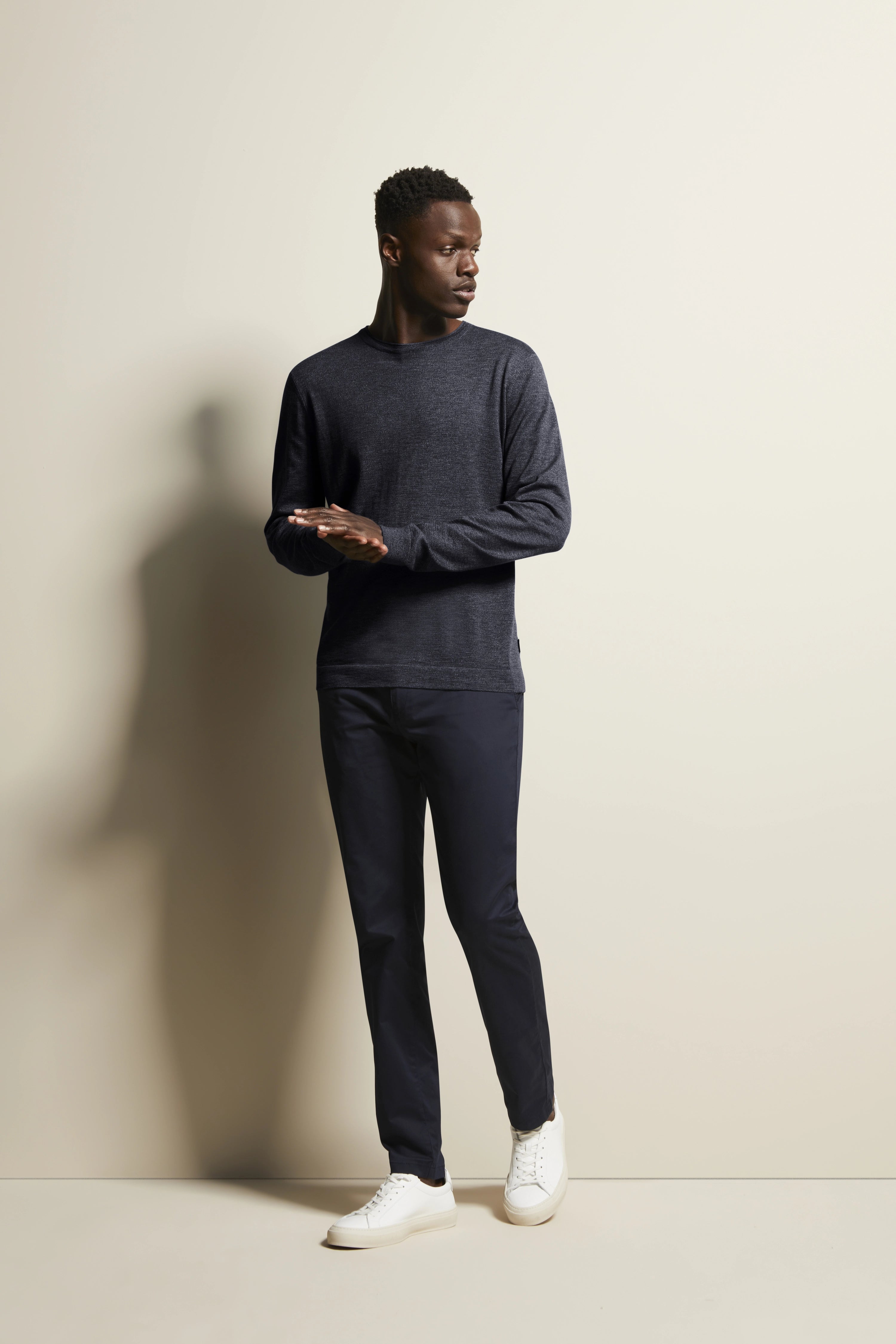 bugatti Modelbild: Navy Langarmshirt, dunkle Hose, weiße Sneaker, entspanntes Posing, seitlicher Blick.