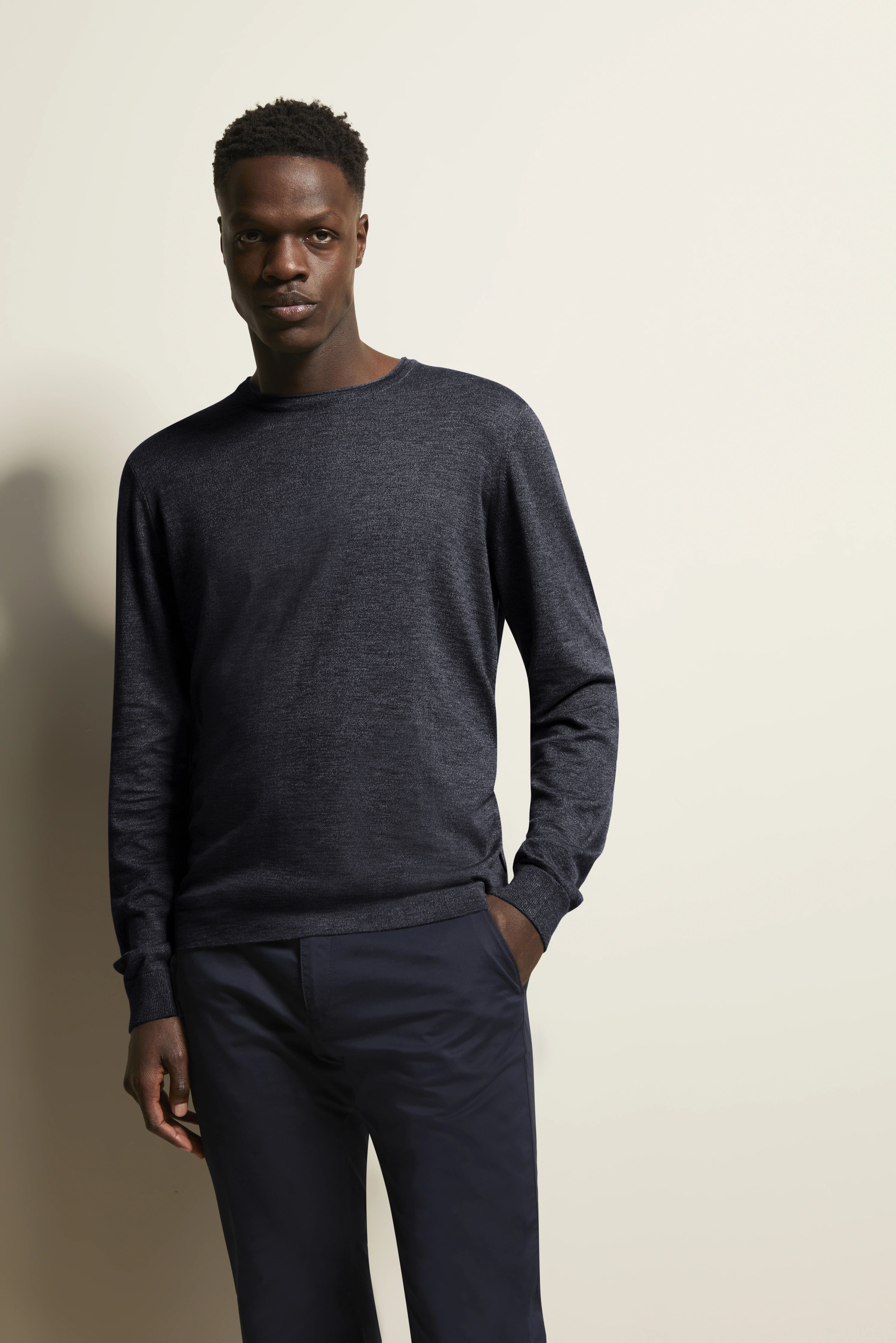 Dunkelblauer Pullover und Hose, Model stehend, Hand in Tasche, bugatti Stil und Eleganz.