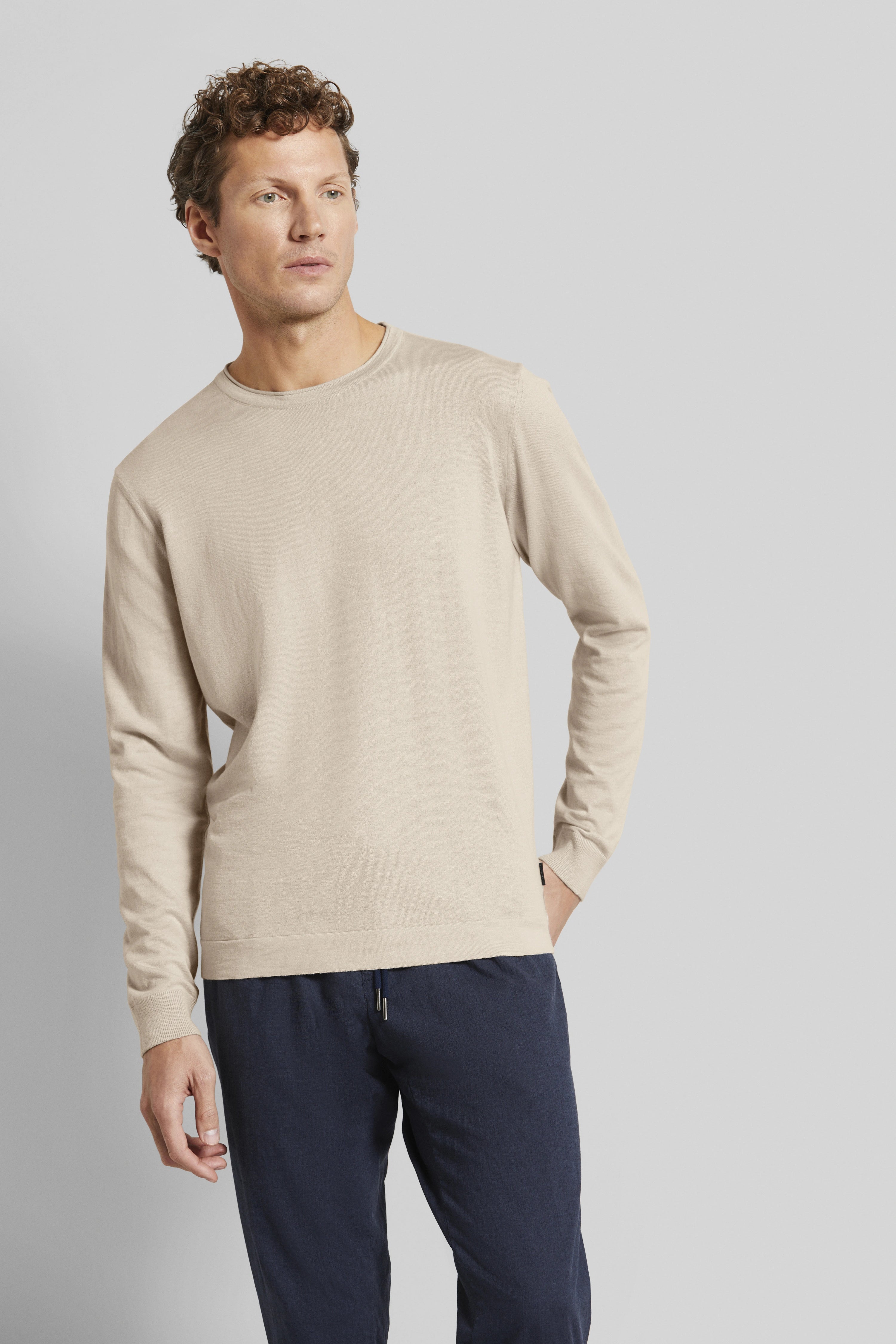Beiges Langarmshirt und dunkelblaue Hose, Modelbild, lässige Pose, bugatti Stil.