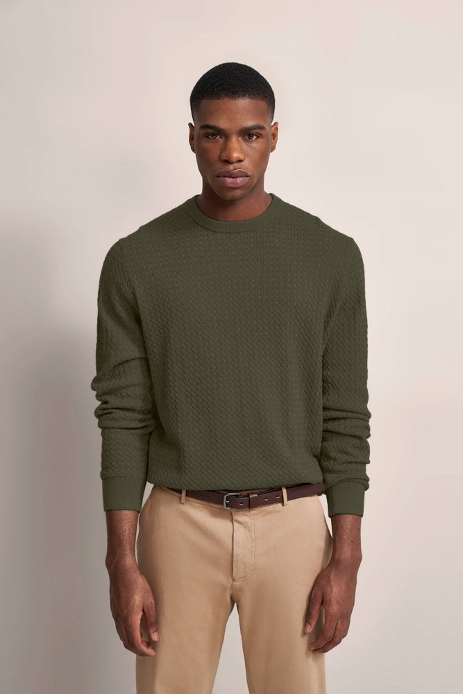 Model in olivgrünem Pullover und beigen Chinos, frontal stehend, legeres Posing.