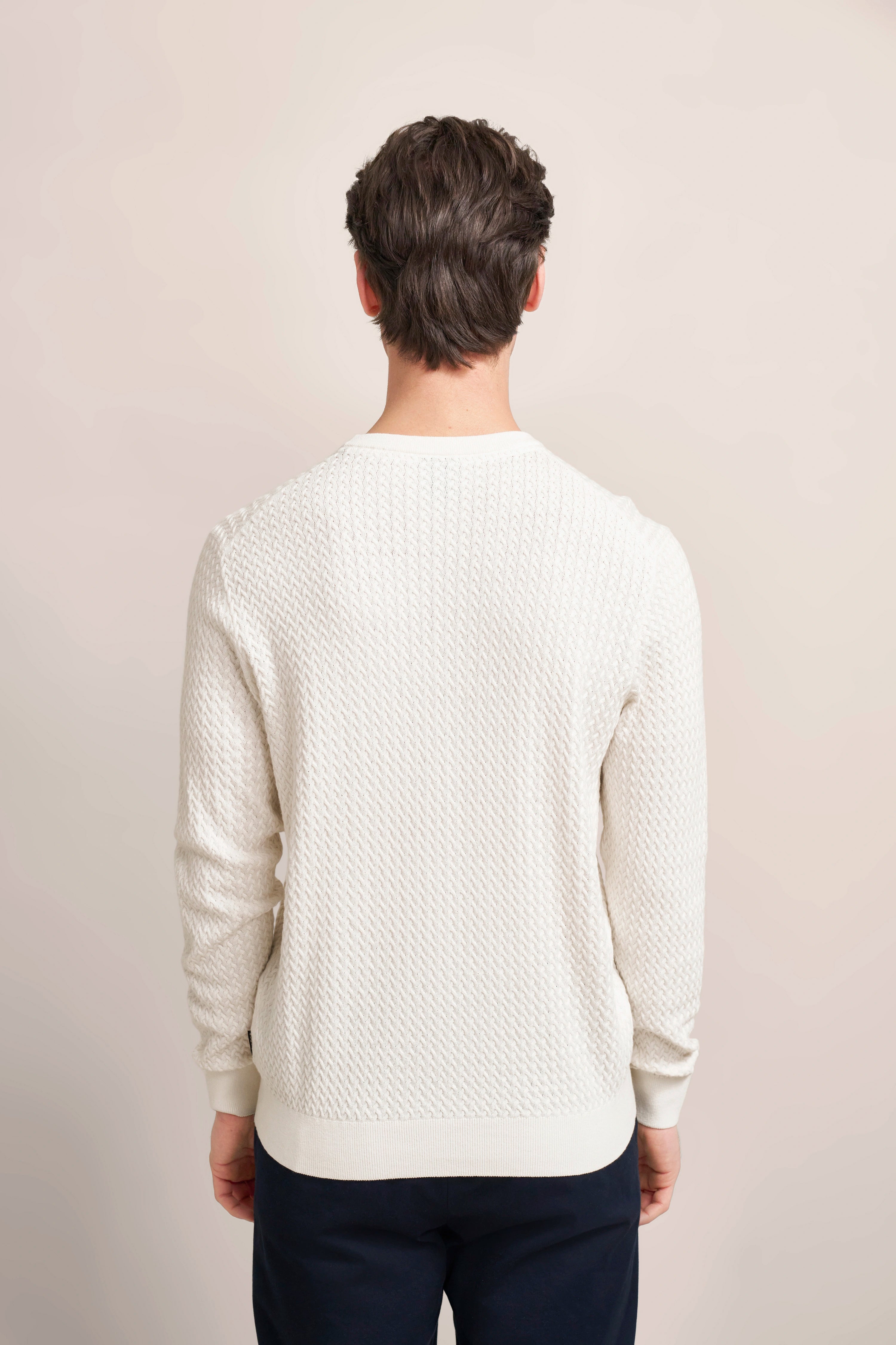 Rückansicht eines Models in cremefarbenem bugatti Pullover mit Strukturmuster, lässige Pose.