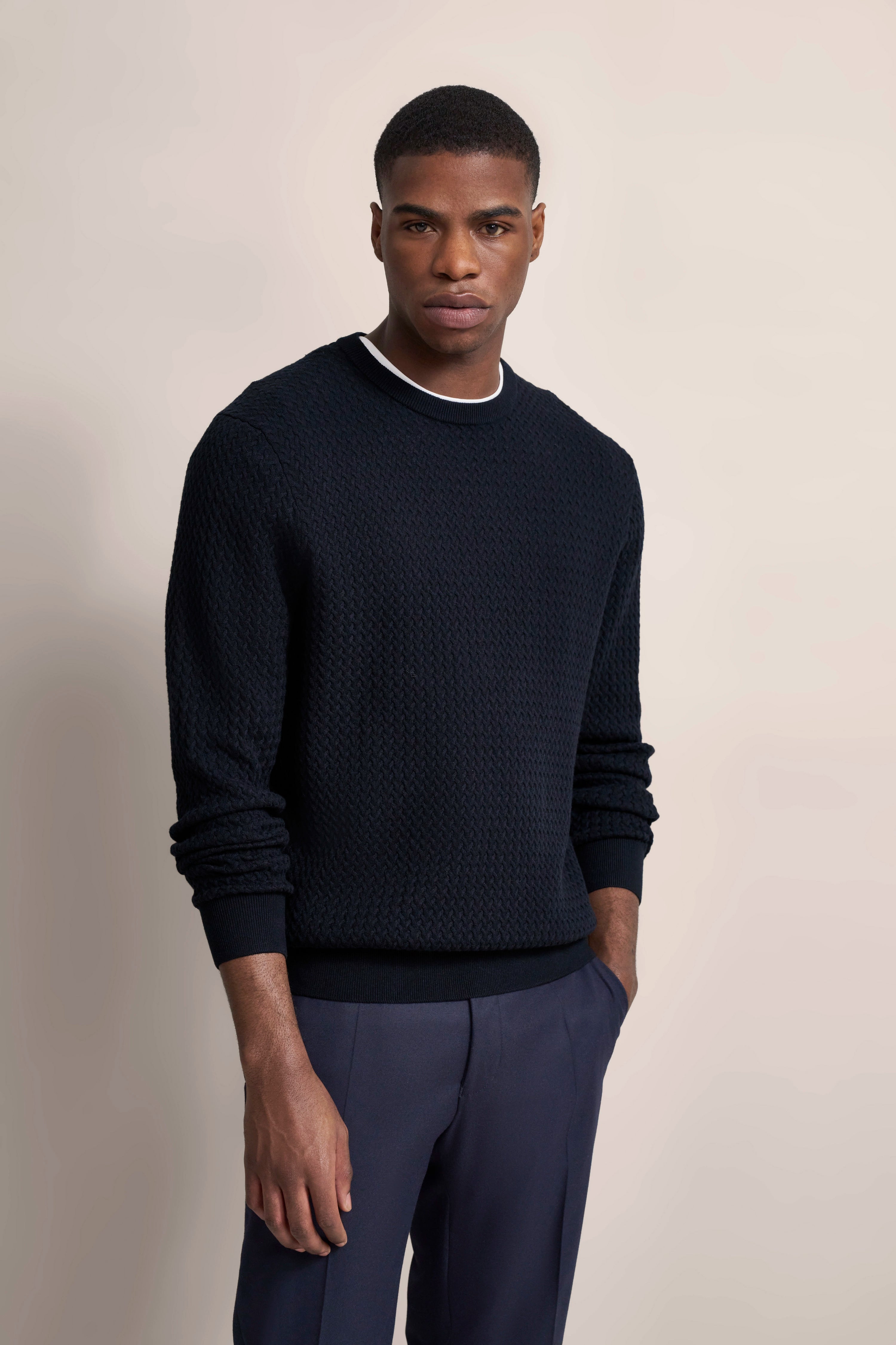 bugatti Modelbild: Dunkelblauer Strickpullover, entspanntes Posing, blaue Hose.