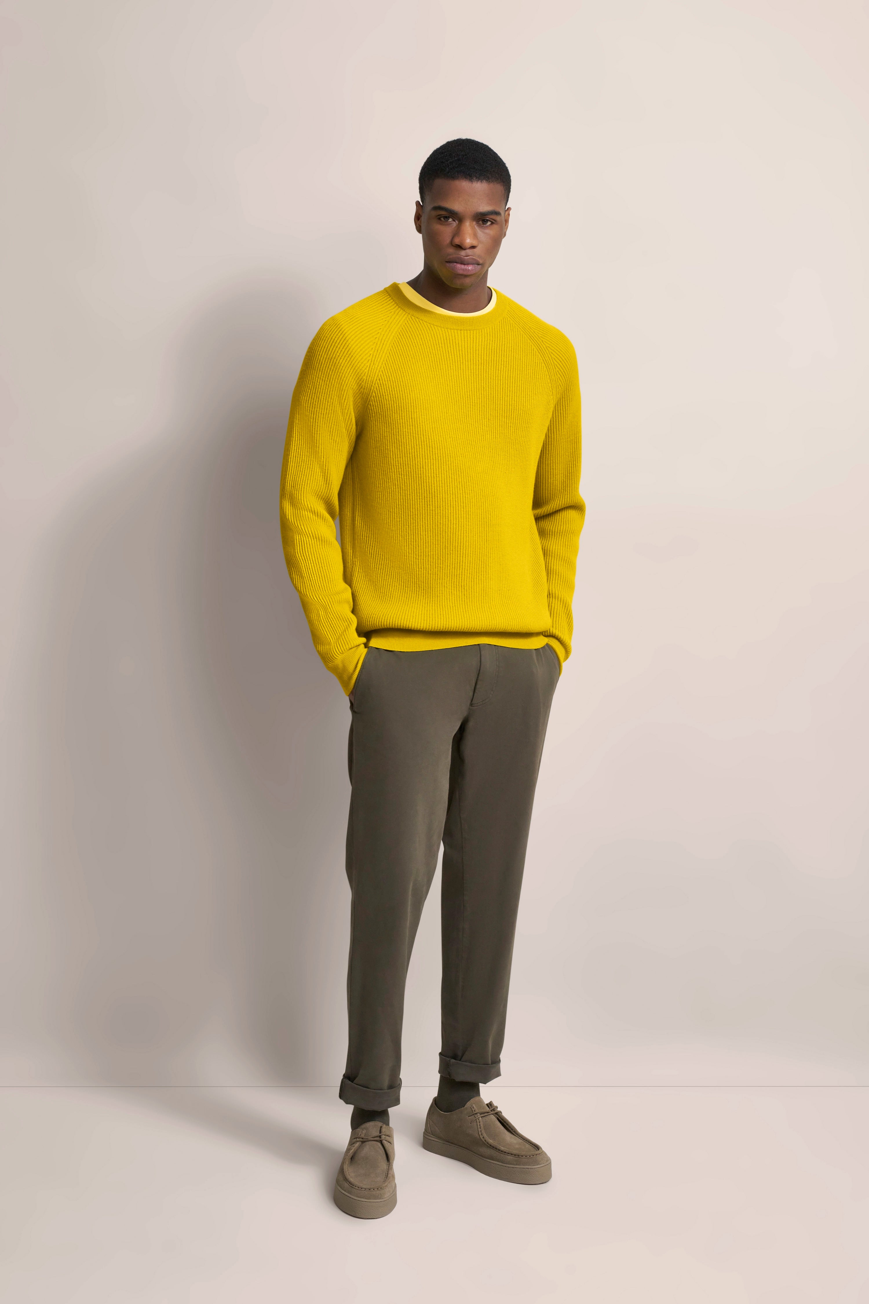 Model trägt gelben Pullover und olivgrüne Hose, legeres Posing, stilvoller Look von bugatti.