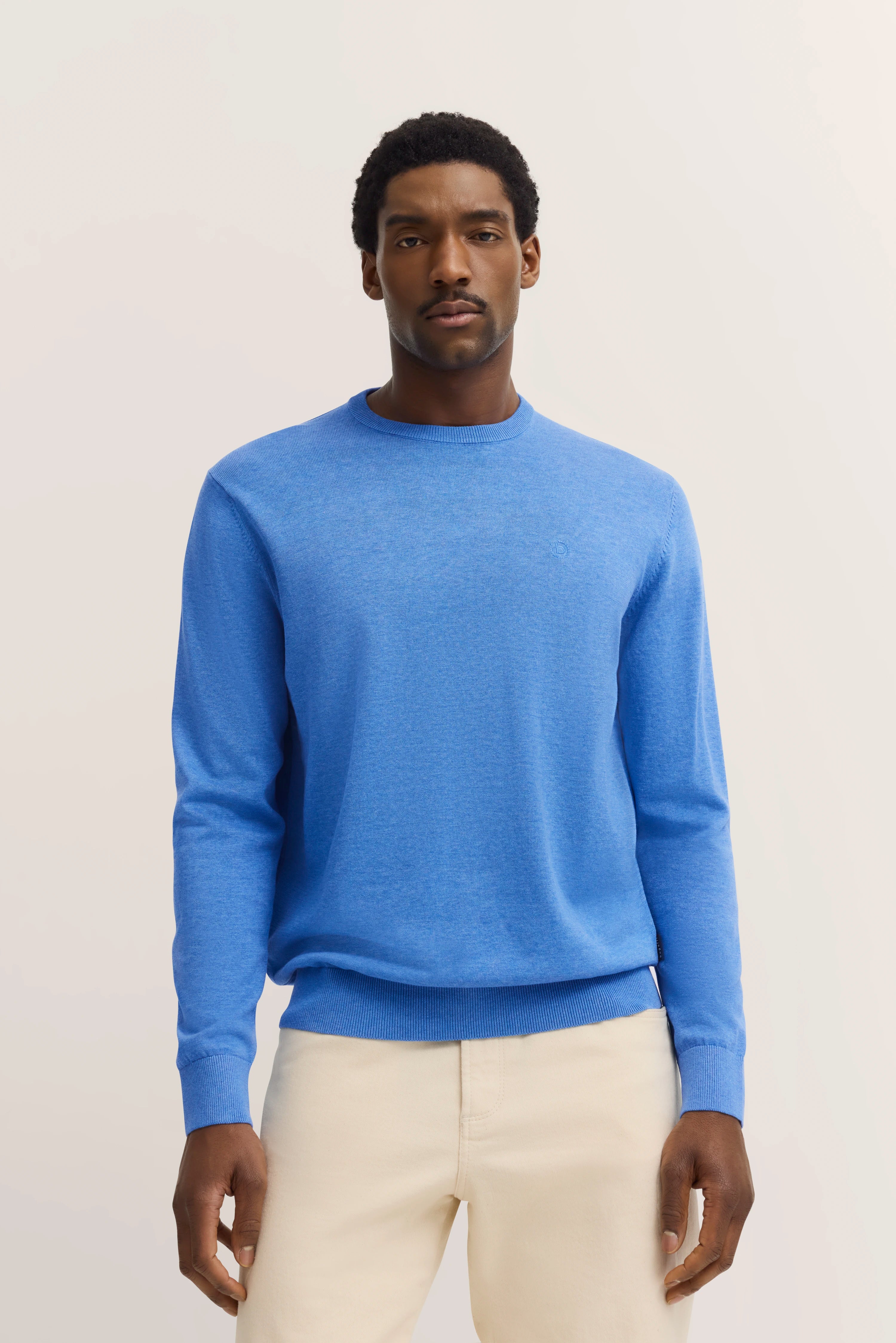 bugatti trui in blauw, modelpose ontspannen, gecombineerd met crèmekleurige broek.