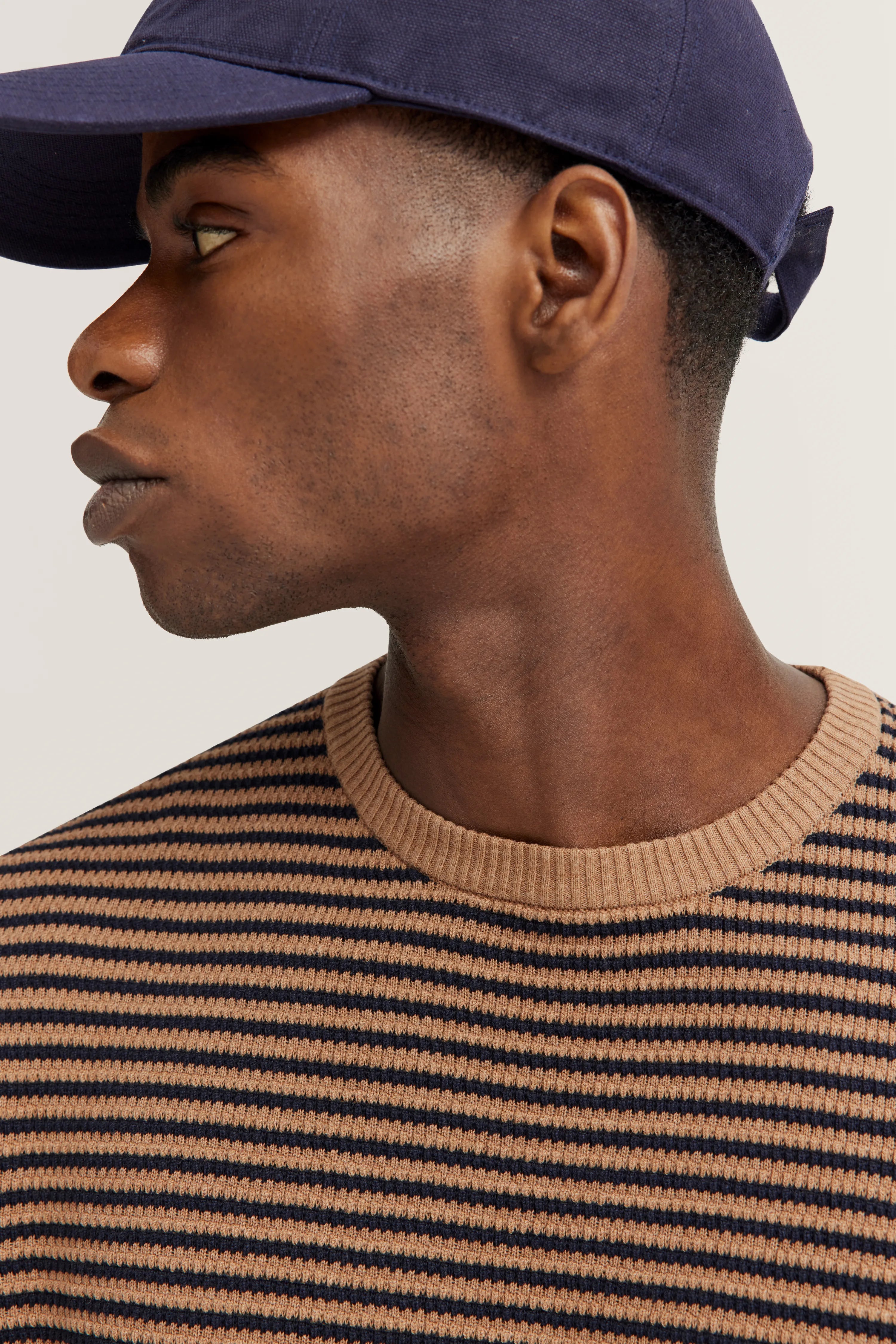 Modell mit marineblauer Kappe, gestreiftem Pullover in Beige und Schwarz, seitliches Posing.