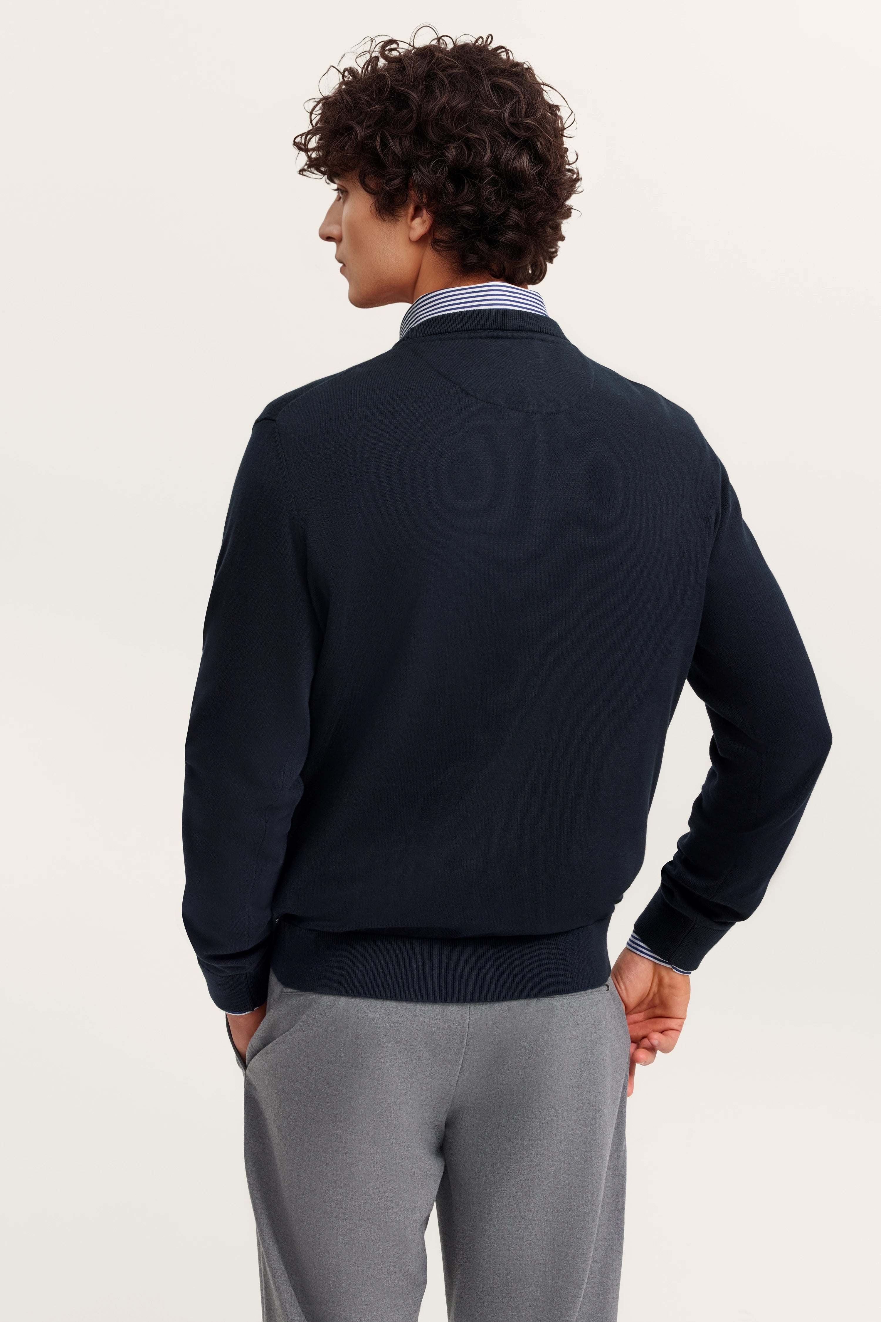 Navy Blazer über gestreiftem Hemd, graue Hose, Model im Seitenprofil.